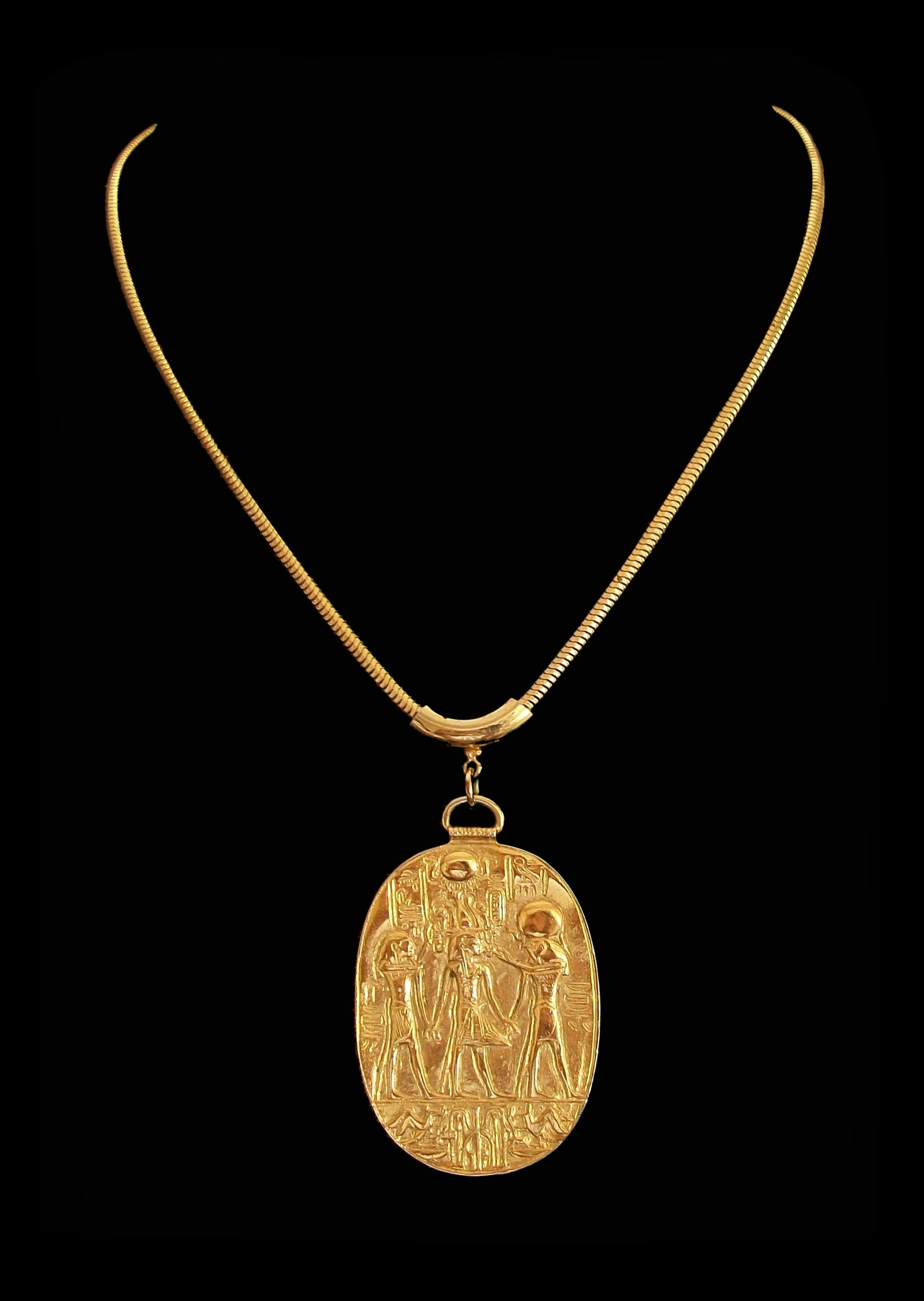 M.M.A. (Metropolitan Museum of Art) - Reproduktion einer ägyptischen Ausstellung, goldfarbenes Collier - mit einem geprägten ovalen Anhänger mit altägyptischer Ikonographie - originale Schlangenkette mit Federringverschluss - signiert auf der