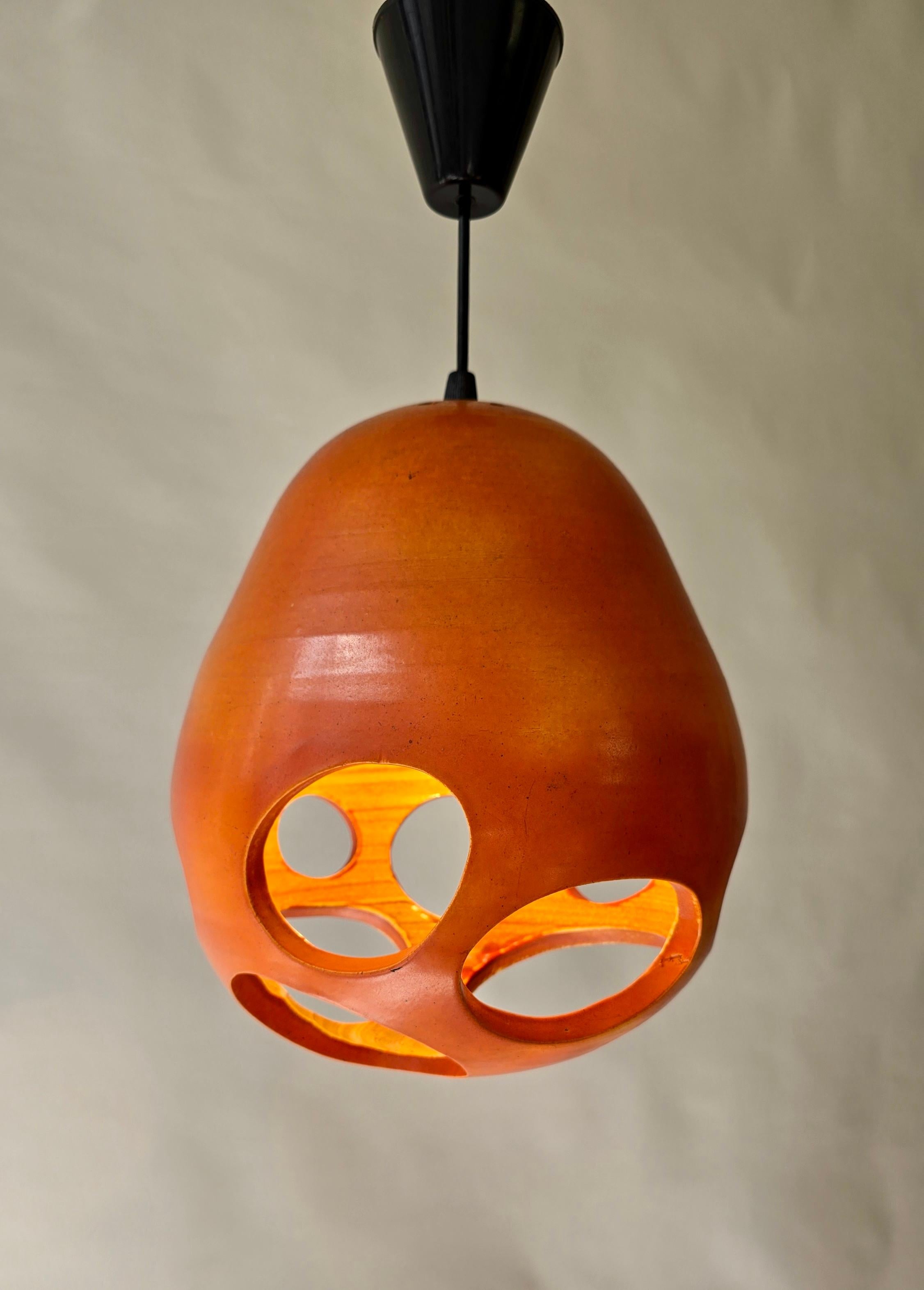 Spettacolare ciondolo olandese con tagli audaci e smalto organico arancione.

Spettacolare pendente in ceramica realizzato a mano da Mobach (Utrecht), risalente agli anni 1960-70. Il paralume biomorfico è drammaticamente traforato con tagli