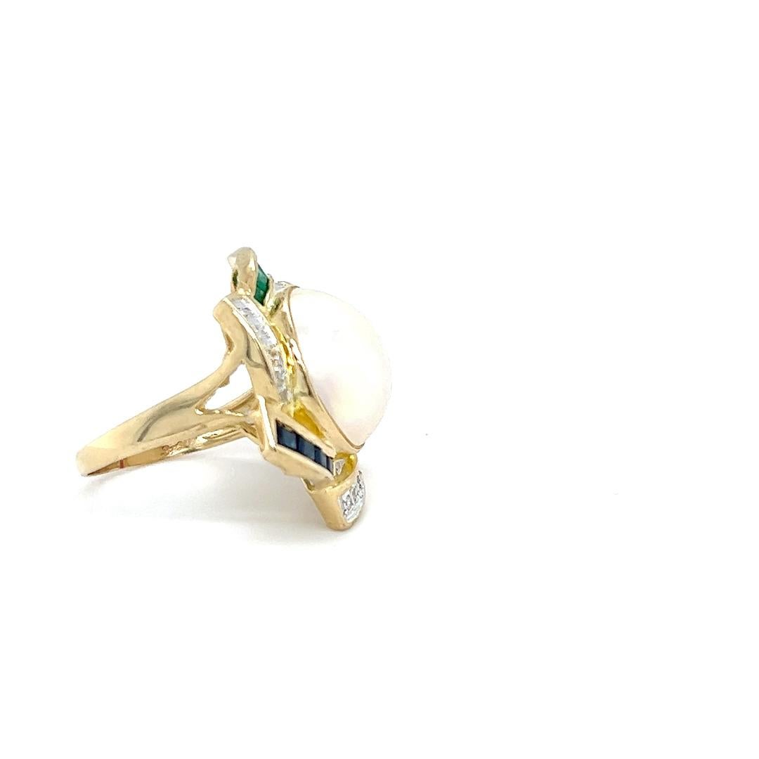 One 14 karat yellow gold ring set with one 14.5mm round white mobe cultured pearl, surrounded by twelve (12) round brilliant cut diamonds, approximately 0.10 carat total weight with matching H/I color and I2 clarity and four (4) square cut emeralds,