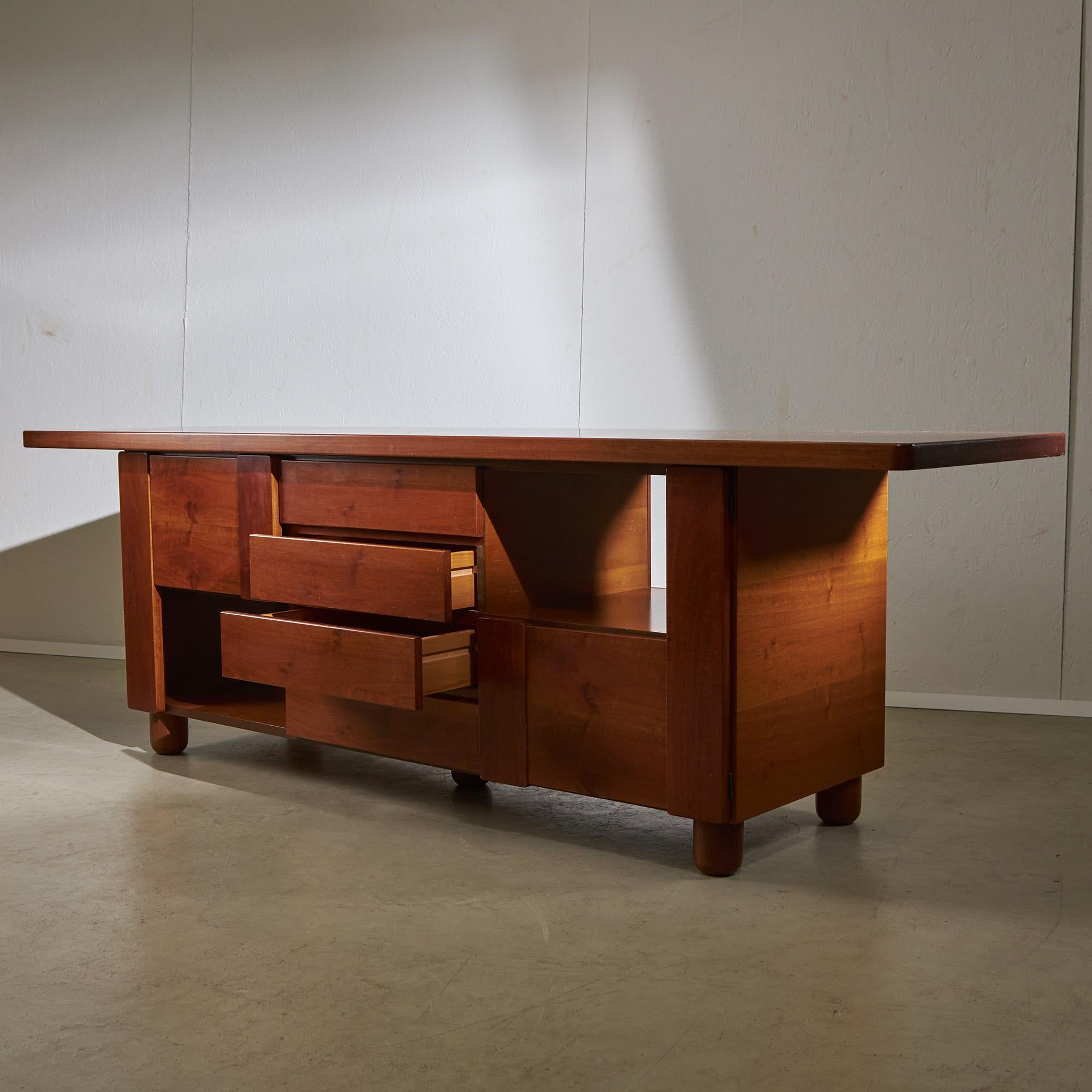 Ti presentiamo un pezzo di eleganza vintage: questa credenza in noce italiana degli anni '70, disegnata per Mobil Girgi. Presenta quattro cassetti centrali che combinano funzionalità e stile e due scomparti aperti sui lati, perfetti per mettere in