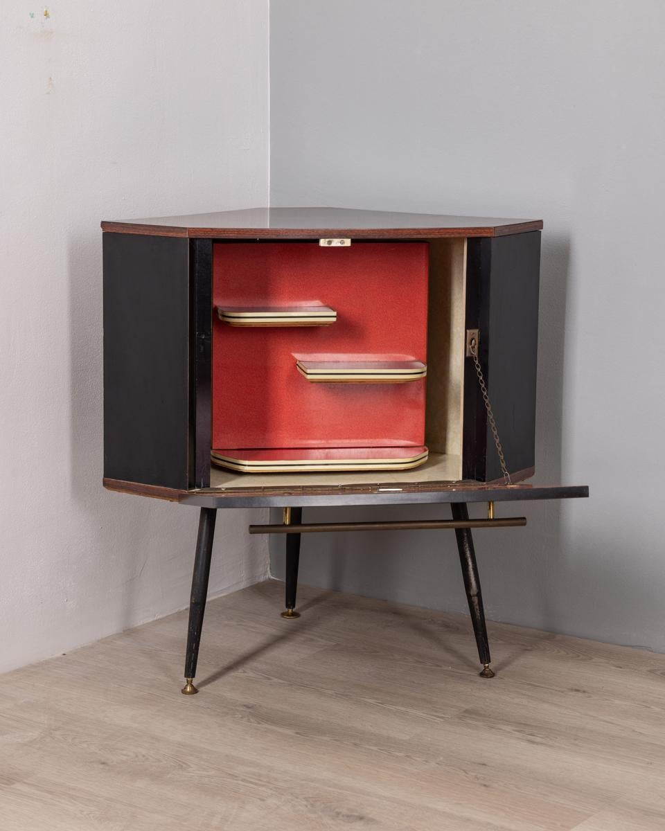 Meuble de bar d'angle, pieds en métal noir et pieds en laiton doré, cadre en bois avec une porte centrale à abattant avec un cadre pivotant à l'intérieur avec des étagères en formica et un miroir, design italien, années 1960.

CONDITION :
En bon
