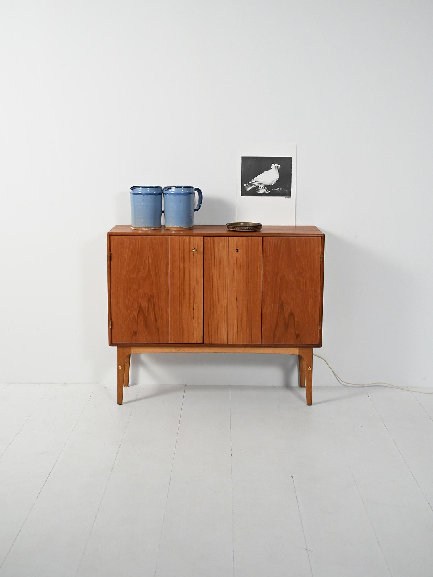 Mobile bar anni ’50 in teak con due ante a soffietto, interno a specchio con vano portabottiglie.

Elegante mobile bar scandinavo anni ’50 in teak con struttura leggera su gambe in rovere tornite e affusolate. Le doppie ante a soffietto celano un