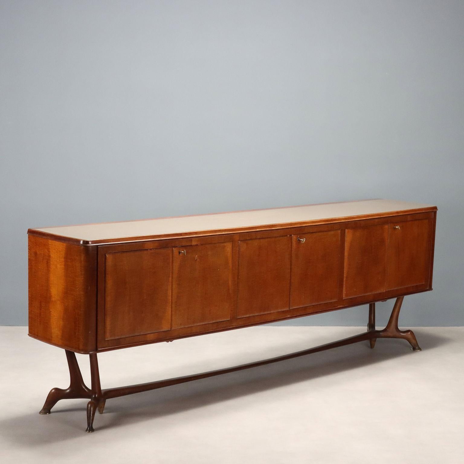 Buffet con puertas batientes, madera chapada en madera de brezo, patas en madera de haya teñida, tapa de cristal con tratamiento posterior. Buen estado, falta el respiradero de la cerradura central.
