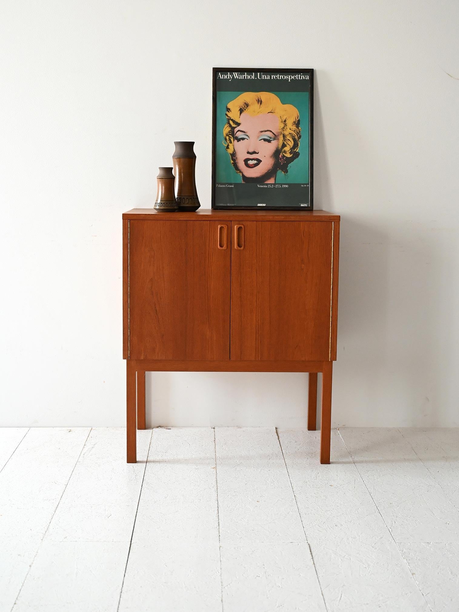 Mueble de almacenaje vintage de teca con puertas batientes y tiradores empotrados. Líneas esenciales y estructura alta sobre piernas esbeltas.

Armario de almacenaje escandinavo de los años 60 fabricado en madera de teca, con puertas batientes y