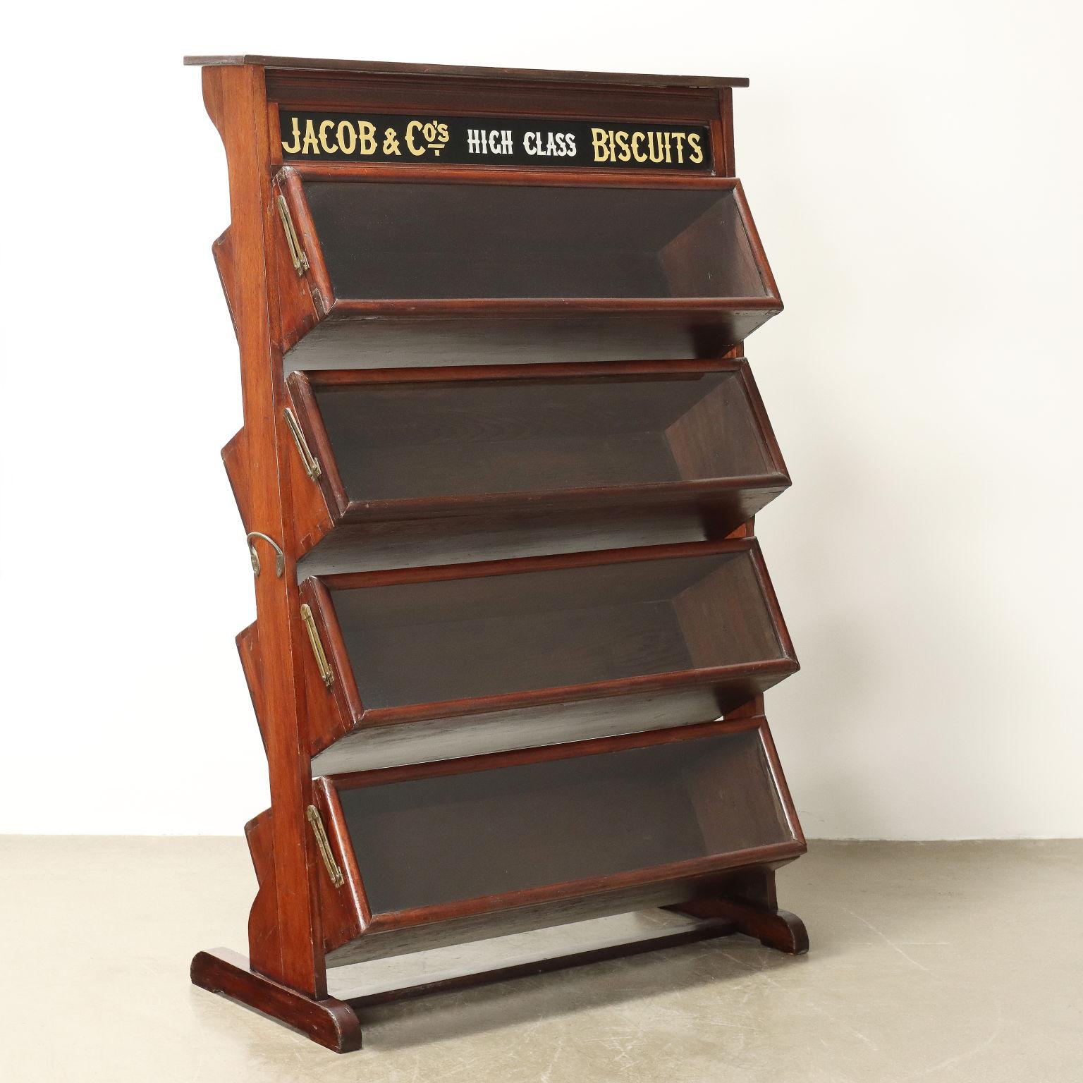 Particular vitrina de época, con inscripción original en inglés y etiqueta del fabricante en la parte posterior, compuesta por compartimentos de almacenaje con puertas de cristal de apertura vertical, fabricada en madera de caoba.