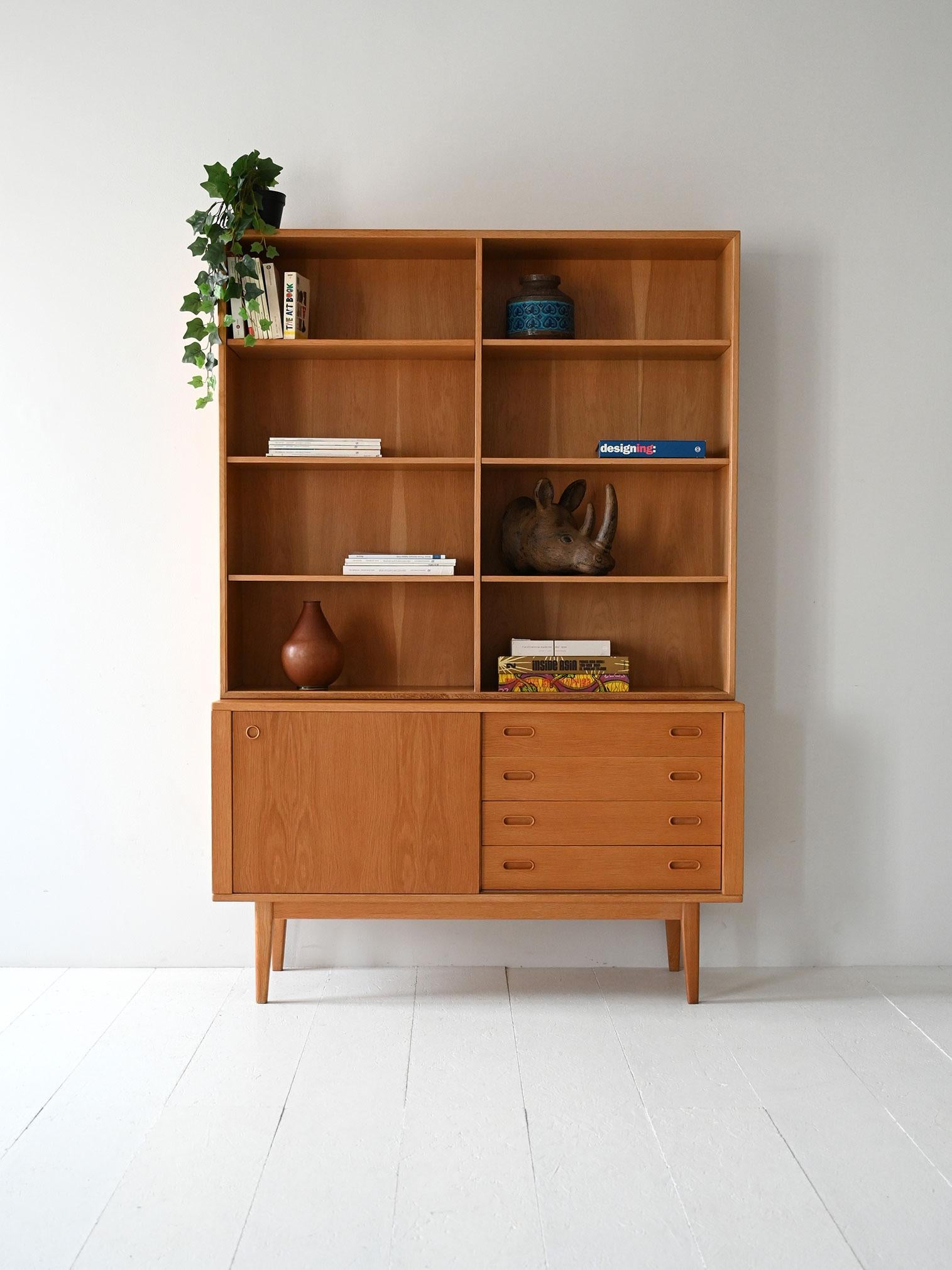 1960s bookcase with exposed shelves, drawers, and storage compartment. Linear structure and light proportions typical of Nordic design.

Scandinavian 1960s bookcase made of light oak. The upper structure features symmetrical exposed shelves, while