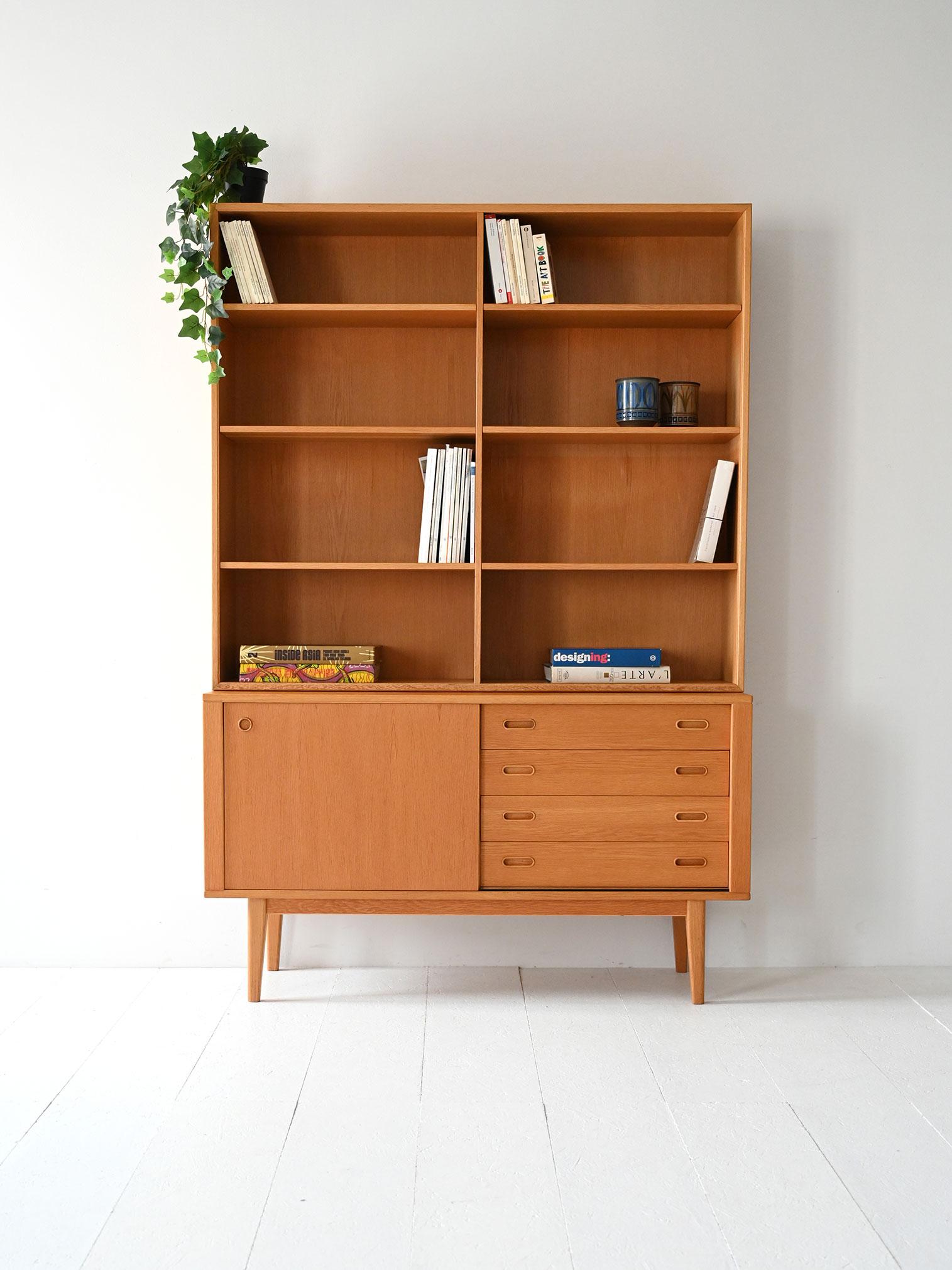 1960s bookcase with exposed shelves, drawers, and storage compartment. Linear structure and light proportions typical of Nordic design.

Scandinavian 1960s bookcase made of light oak. The upper structure features symmetrical exposed shelves, while