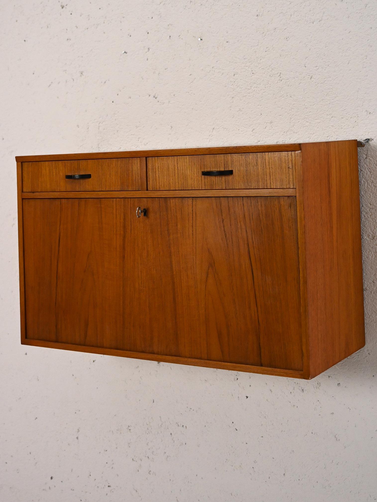 1960s teak wall cabinet with drop-down doors.

An original vintage container as beautiful as it is practical. Due to the presence of the two small drawers and the flap door, it can be used as additional space for different spaces and needs. Try it