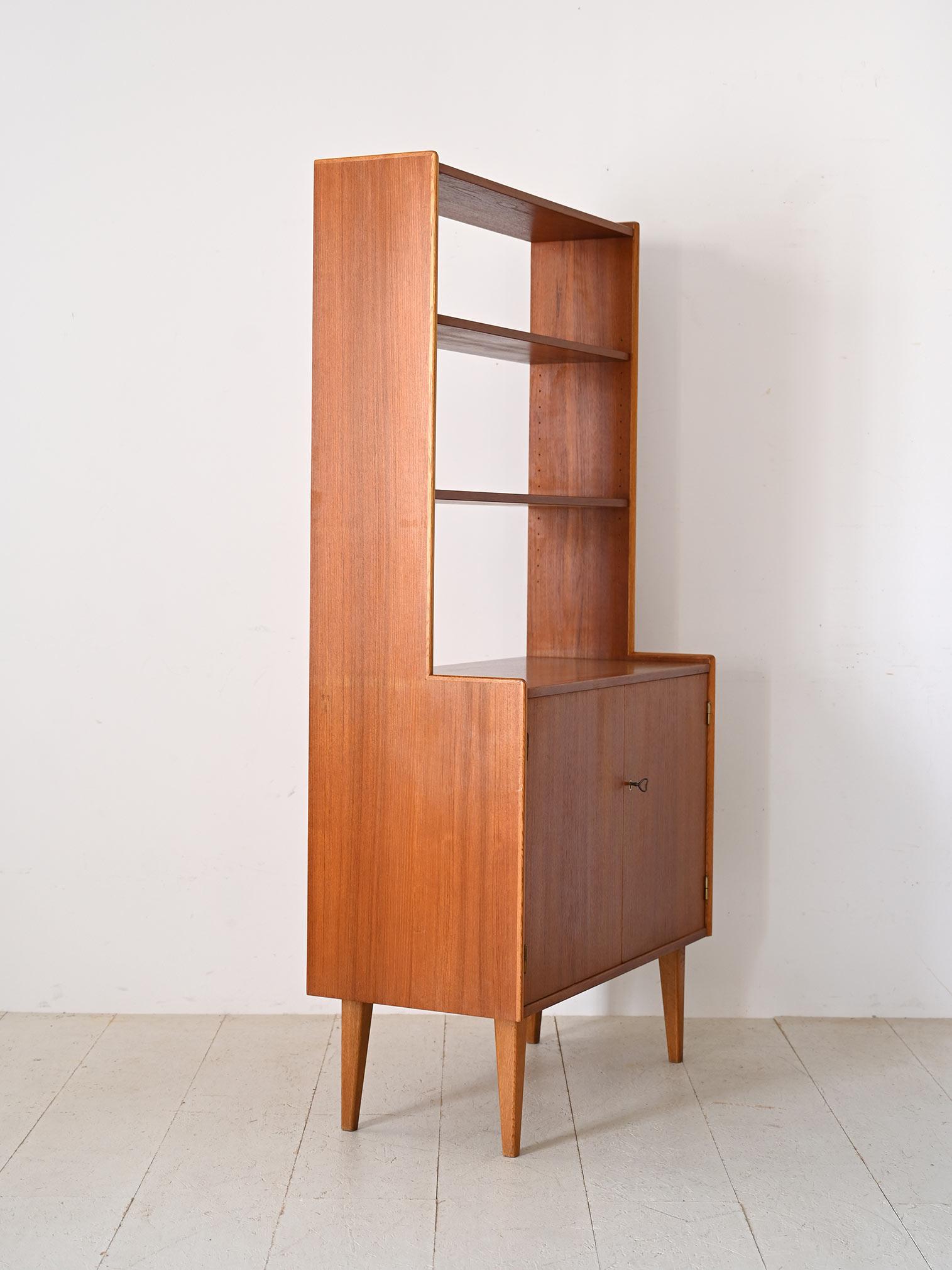 Scandinavian teak bookcase from the 1960s.
The lower part has a large compartment closed by two hinged doors, while the upper part is divided into two sections: two open shelves and two small drawers.
The essential design and clean lines, typical of