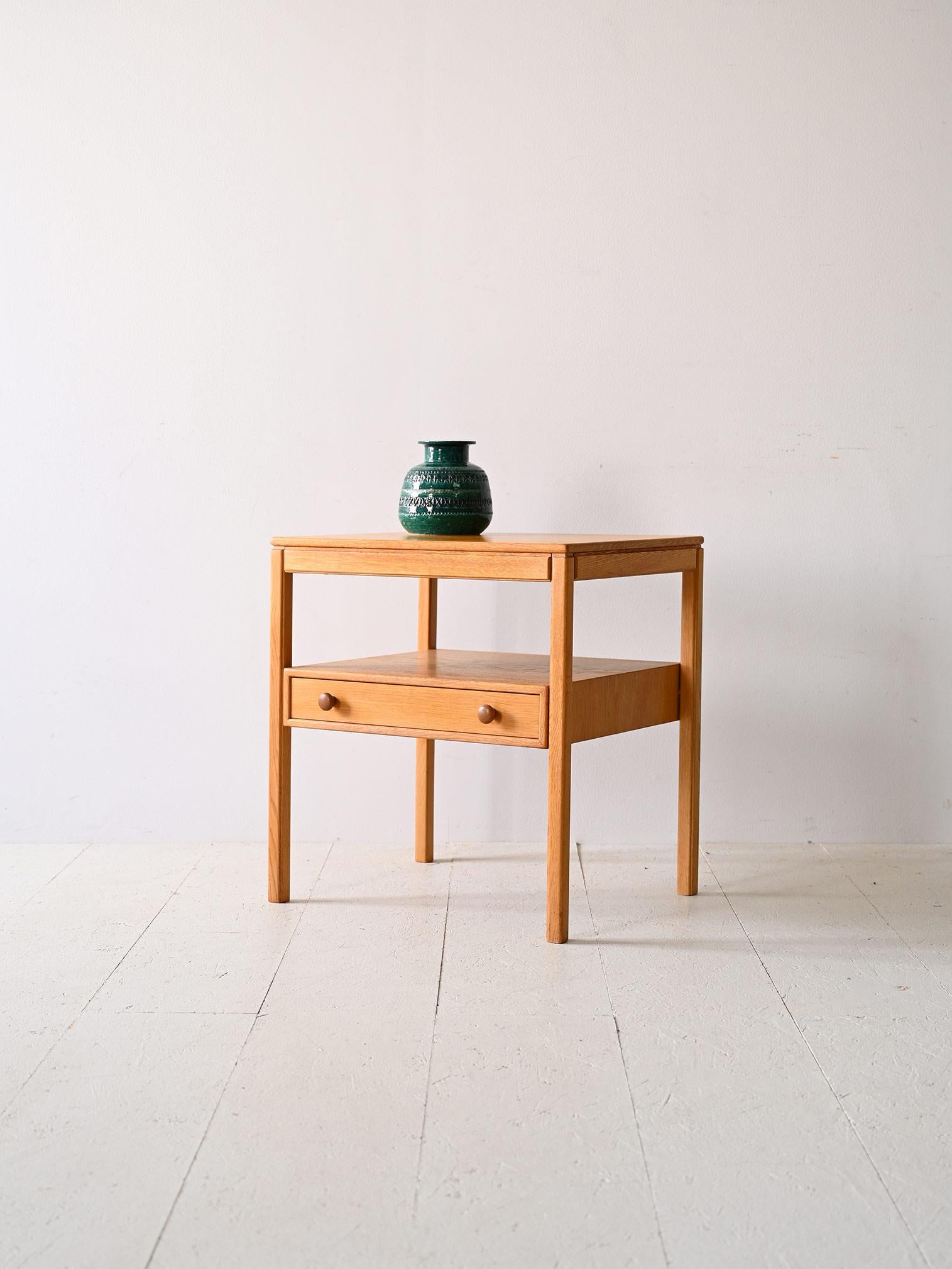 Originaler Nachttisch aus nordischer Eiche im Vintage-Stil.

Es ist aus Eichenholz gefertigt und hat eine raffinierte Struktur mit dünnen, quadratischen Beinen, die dem Möbel einen leichten Touch verleihen. Die Schublade mit ihren runden,