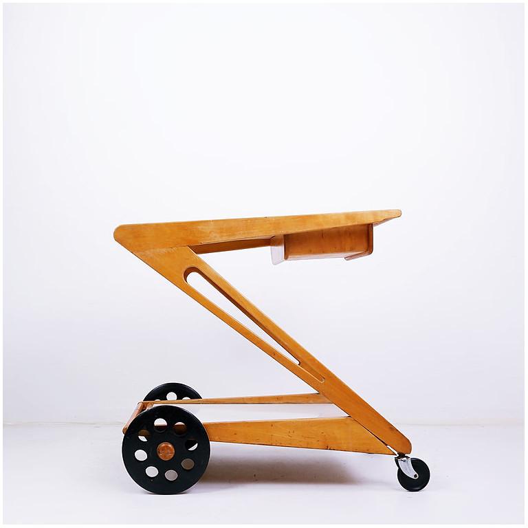 Elegant and hard to find trolley. Maple/oak wooden Z-shaped frame with two laminated trays. The top tray can slide open and/or be removed to reveal a small wooden serving basket underneath. Black ebonized wheels back and small rotating wheels at
