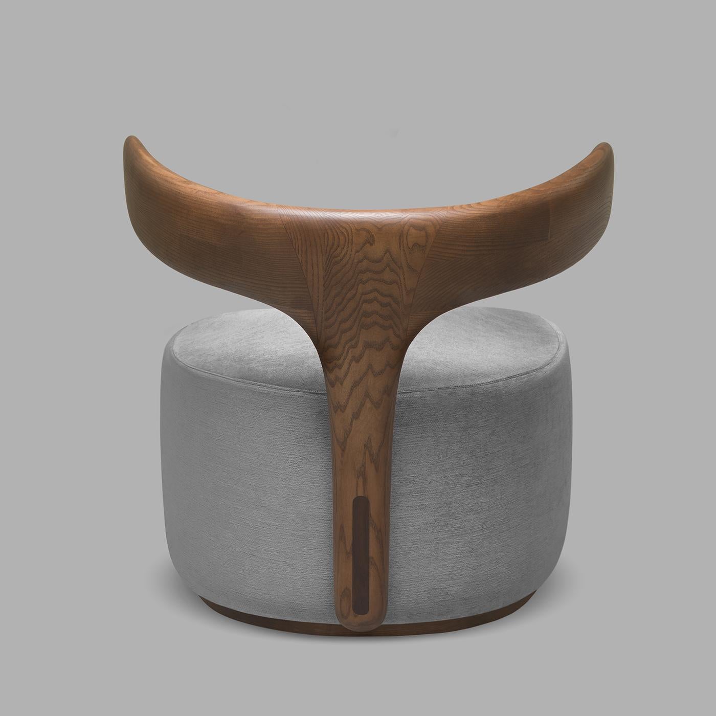 Moby Dick is an armchair with an iconic and enveloping ash backrest evoking a whale tail. The armchair is made of walnut ash wood with a structure that recalls the tail of a whale. The seat is padded and covered in gray fabric. Thanks to its