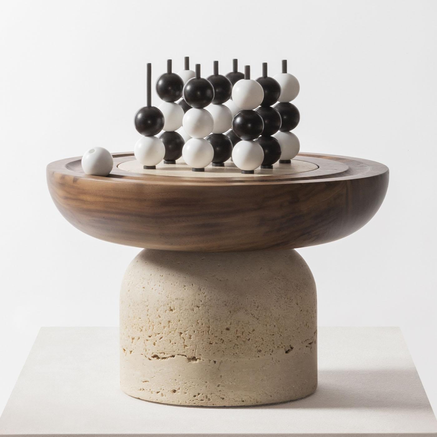 Large volumes in wood and stone are carved and sculpted to create playing fields with modeled, almost primitive lines, with a solid walnut top on a travertine base, designed by Simone Facciullacci. Bakelite black and white beads and burnished