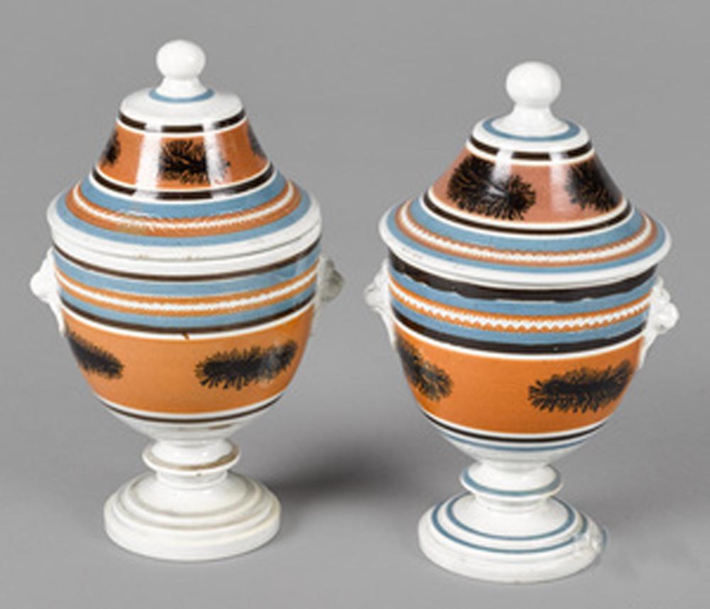 Mocha pottery covered urns with lion-head handles,
circa 1825
(Ny9364-crrr)

An unusual pair of mocha urns and covers with a series of slip bands encircling the pots and covers of brown and blue and large central bands in ochre with dendritic