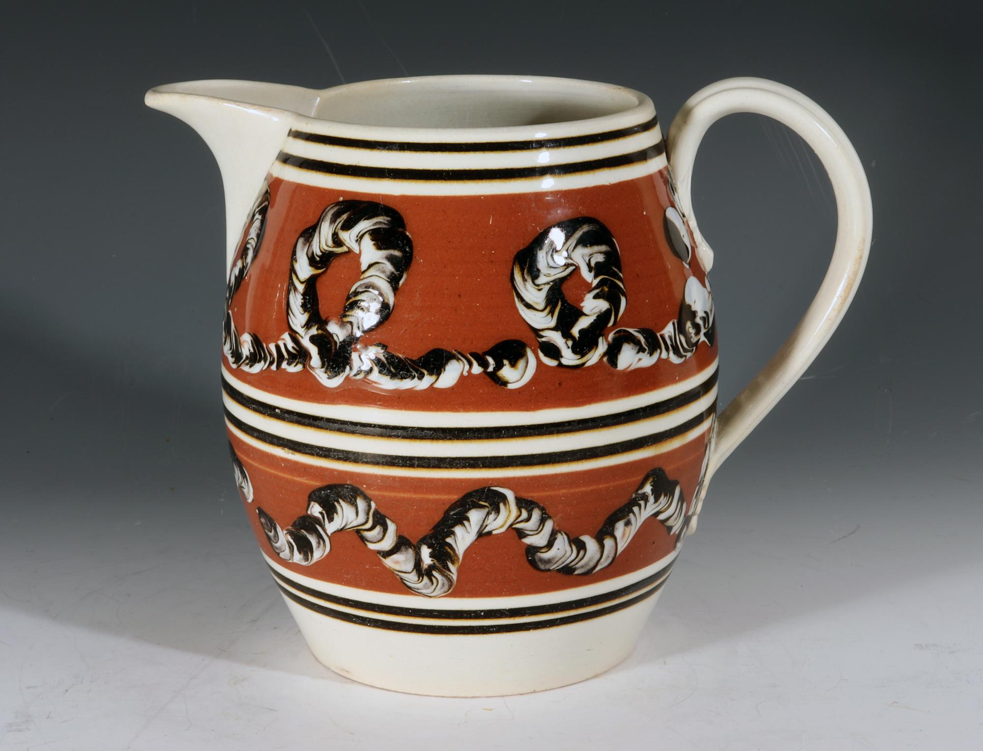 Mocha Pottery Earthworm Jug,
circa 1820

The mocha pottery jug has two wide ocher bands each with an earthworm design. The top with a looping design and the lower one with a wavy design. To the top, bottom and center are thin brown lines- three