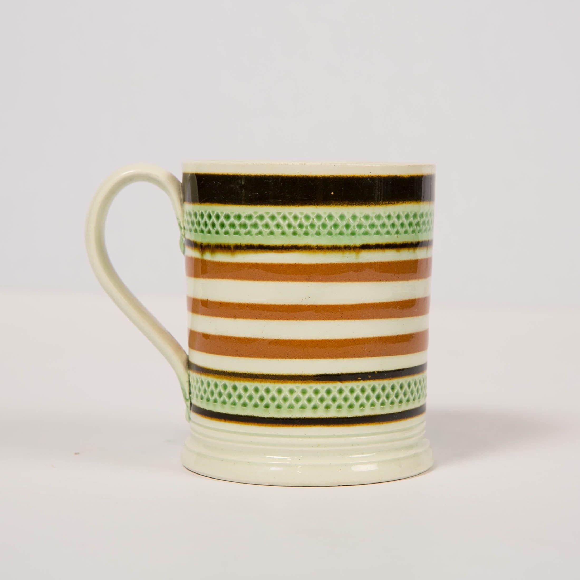 We are pleased to offer this beautiful Mochaware mug, which was turned on a lathe and decorated with slip bands of light and midnight brown. Bands of impressed green glazed diamonds can be seen along the top edge and along the bottom of the mug. The