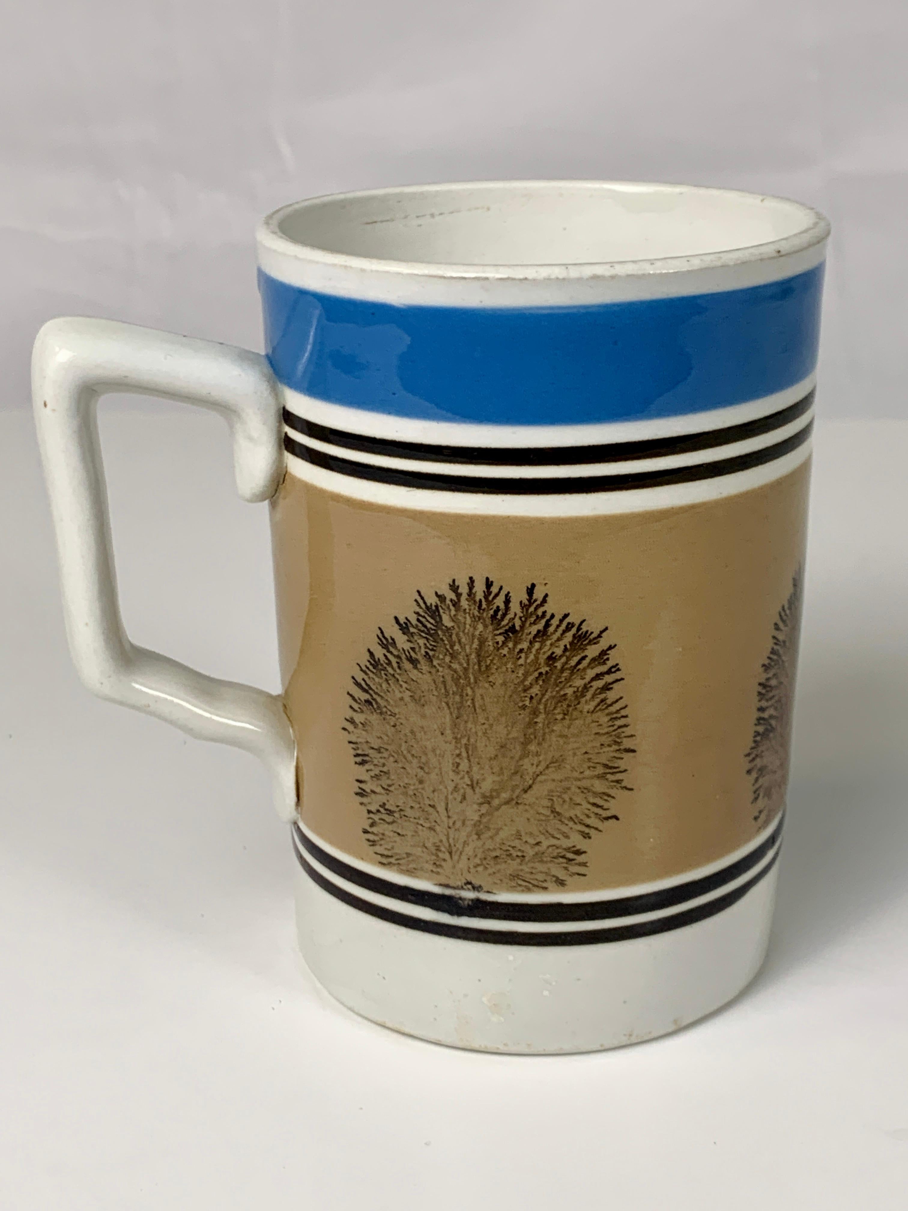 This style of mochaware mug was among the most popular throughout the 19th century. The mug is decorated with blue and beige bands of slip and further decorated with an all-around design of mocha 