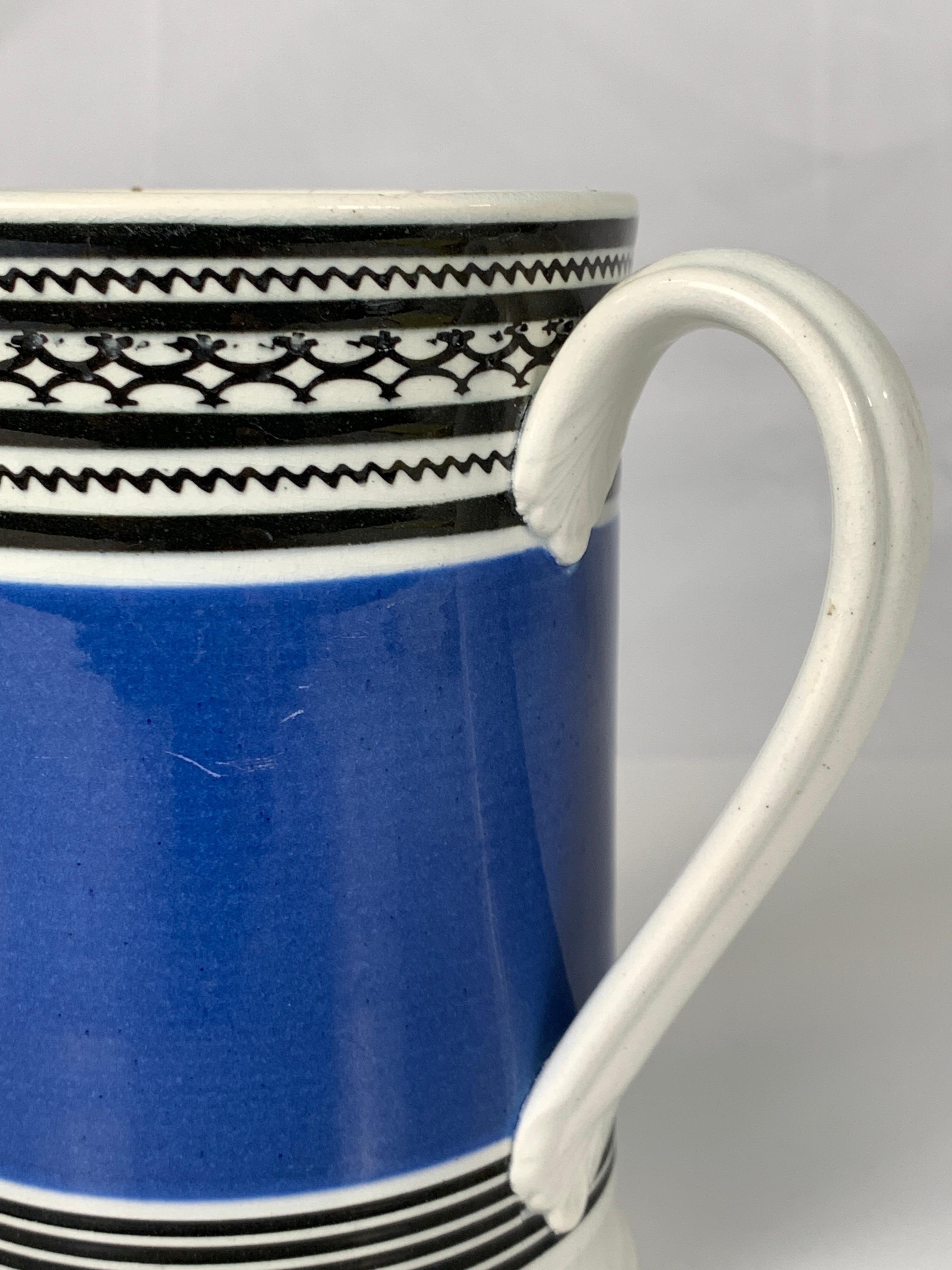 This English mochaware mug is decorated with a wide band of deep royal blue. Above and below the blue are thin black bands, several of which have geometric designs. The body of the mug is pearled creamware which dates the piece to circa 1820.
The