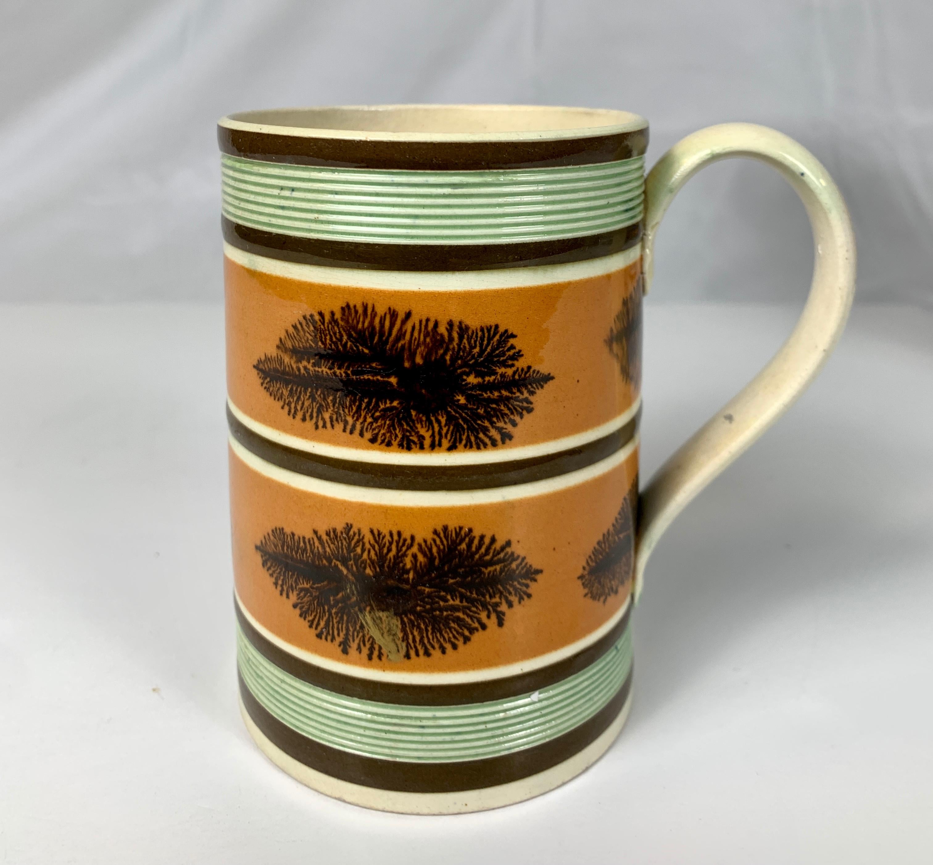Made in England circa 1810, this exquisite mug is decorated with two orange-colored slip bands. Each band is decorated with midnight brown 
