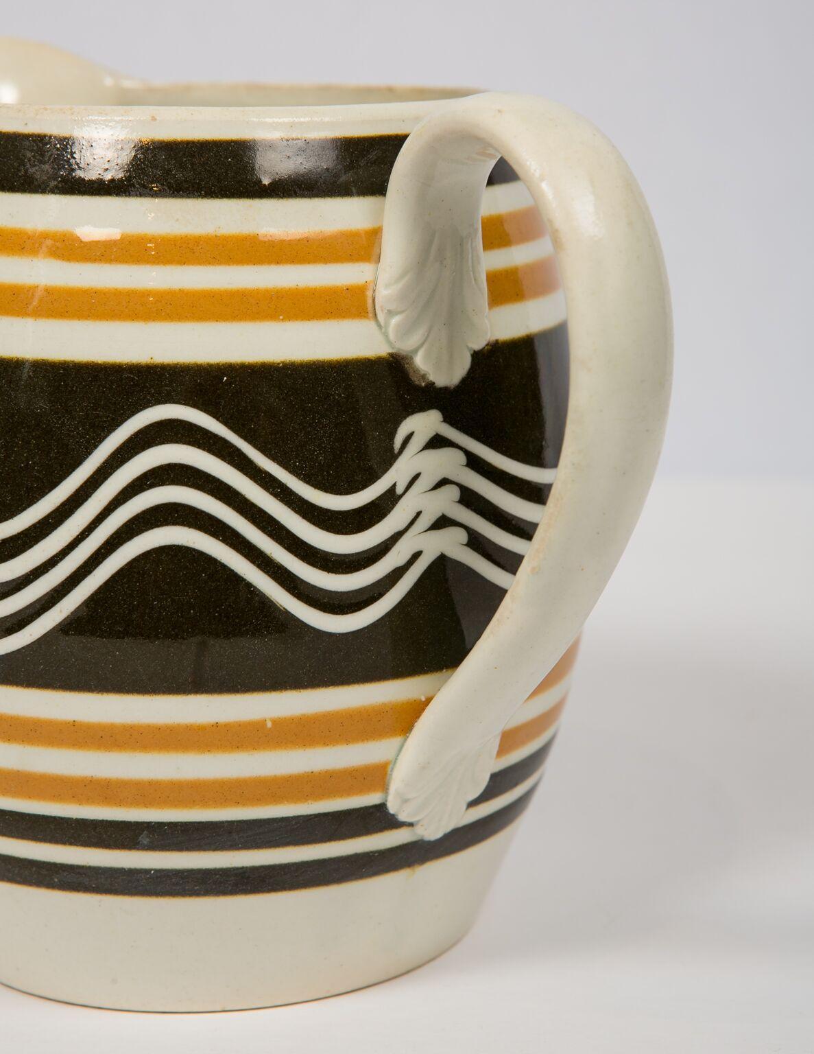 Mocha ware Pitcher. Made in England, circa 1810. Decorated with light and dark brown slip and slip trailing with a single cream color cup with four quills. The strong contrast between the cream-colored wavy lines and the black slip colored ground is