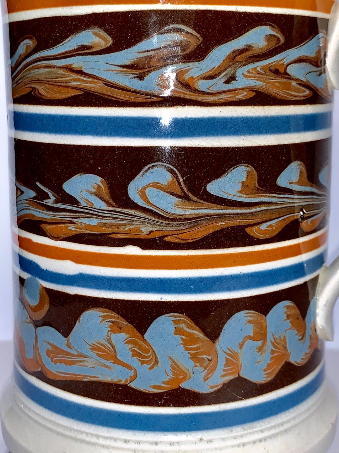 We are excited to offer this quart mocha ware mug made in England, circa 1840.
This mug is decorated with three cables of two colors light blue and light brown on a midnight brown ground. (This is the first time we have had a piece of mocha ware