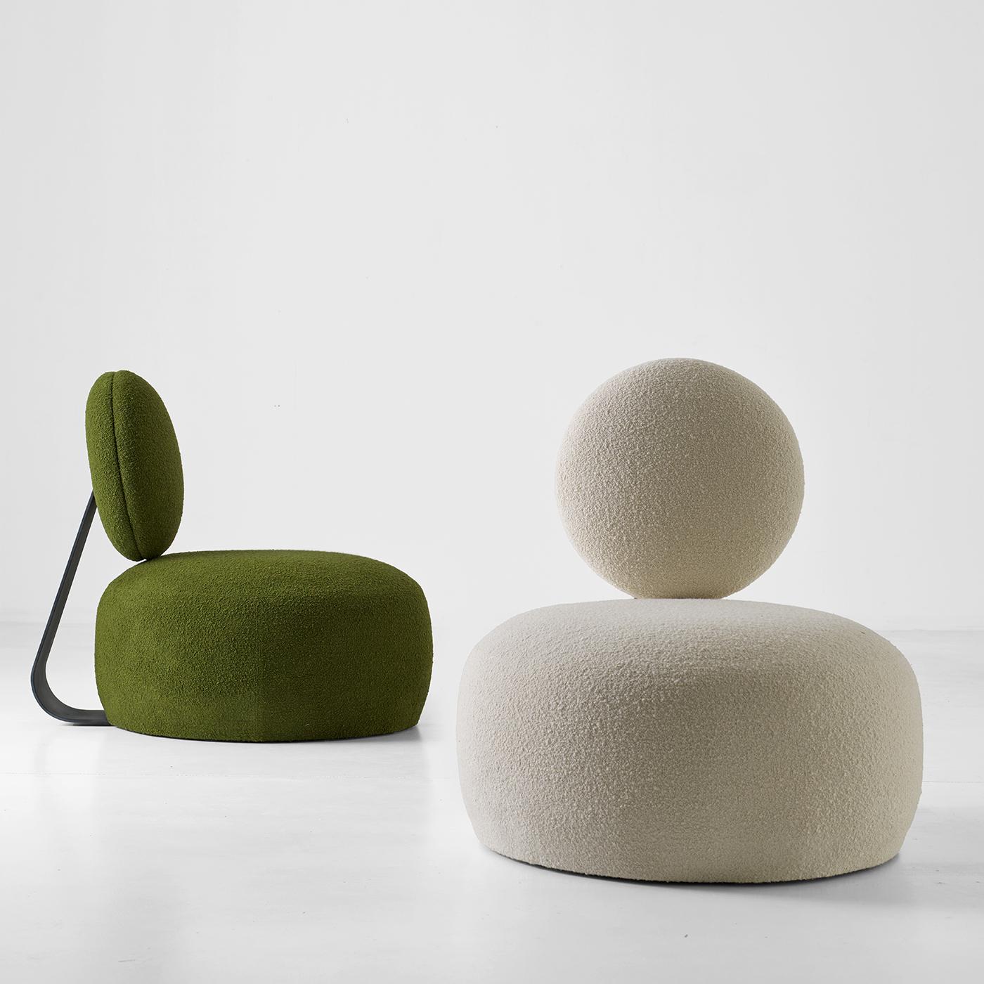El sillón Mochi presenta una silueta suave y acogedora, con un característico respaldo redondeado apoyado en una robusta estructura metálica con acabado champán. Tapizada en un tejido bouclé texturizado, ofrece tanto comodidad como una refinada