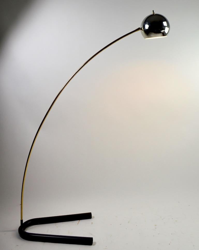 Mod style arc lamp with chrome ball hood shade, brass arm and black finish tubular steel base. The ball shade (6.5 in pivots and tilts to position, and direct the light). Original, clean and working condition, this lamp accepts a standard screw in