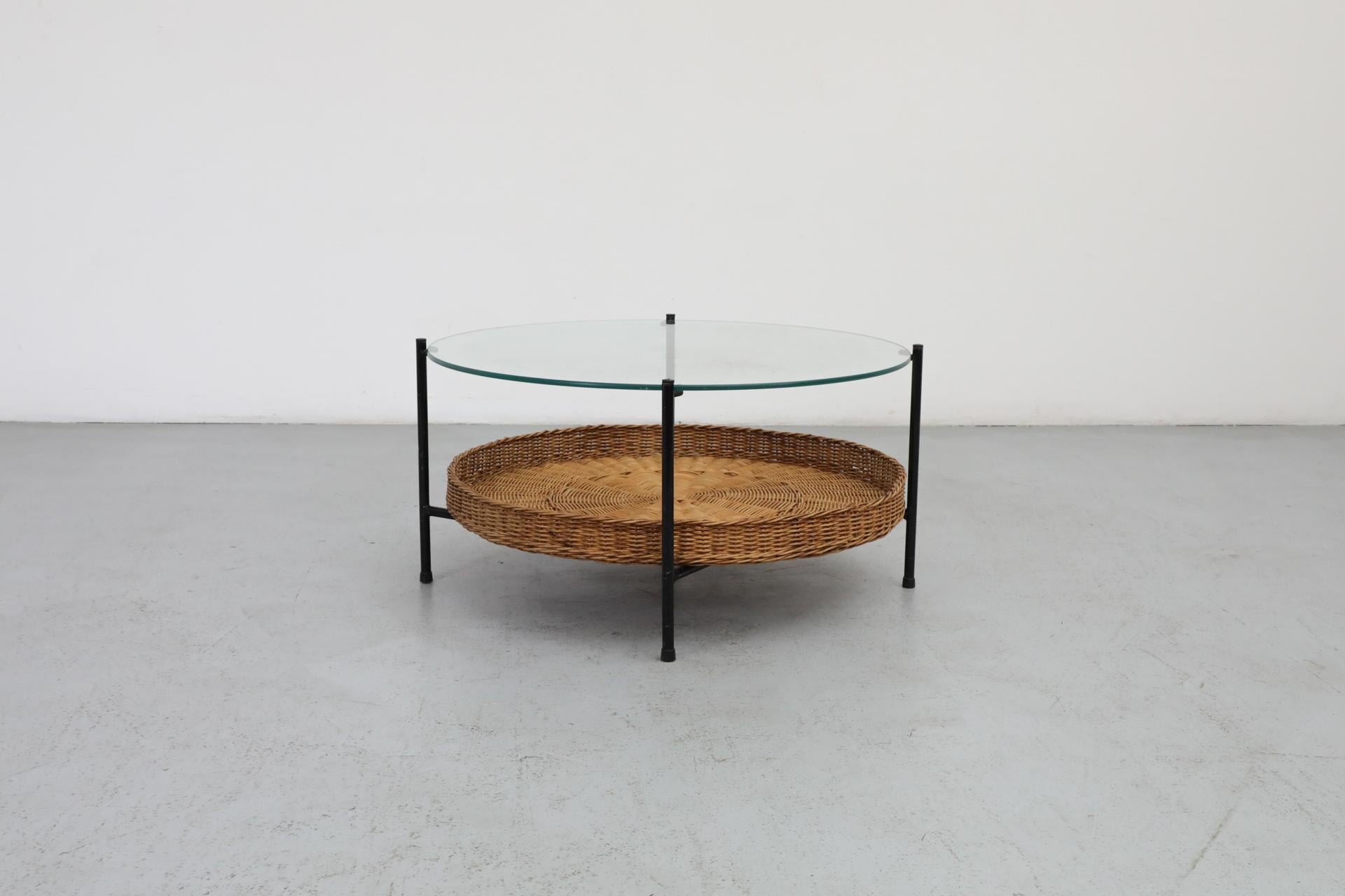 This Dutch Mid-Century, low coffee or side table has a clear glass top and black enameled tubular steel legs. The frame holds a round woven rattan basket under the glass for magazine display or other storage. The glass top is in very original