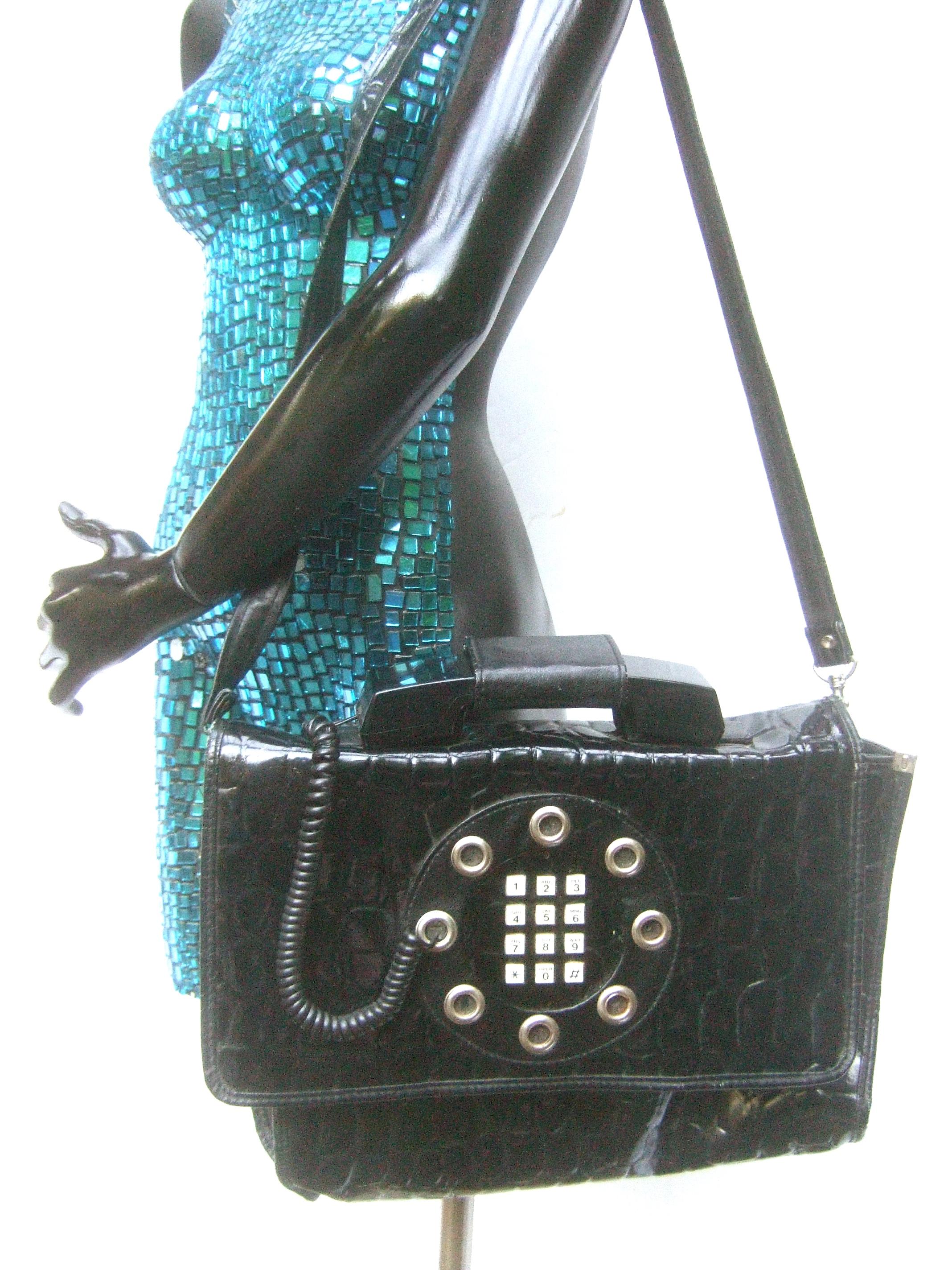 Mod avant-garde embossed black vinyl large shoulder bag c 1980s
The large scale embossed vinyl attache style bag is designed with a telephone receiver on top that serves as the handle. The front exterior has a push-button numerical telephone key pad
