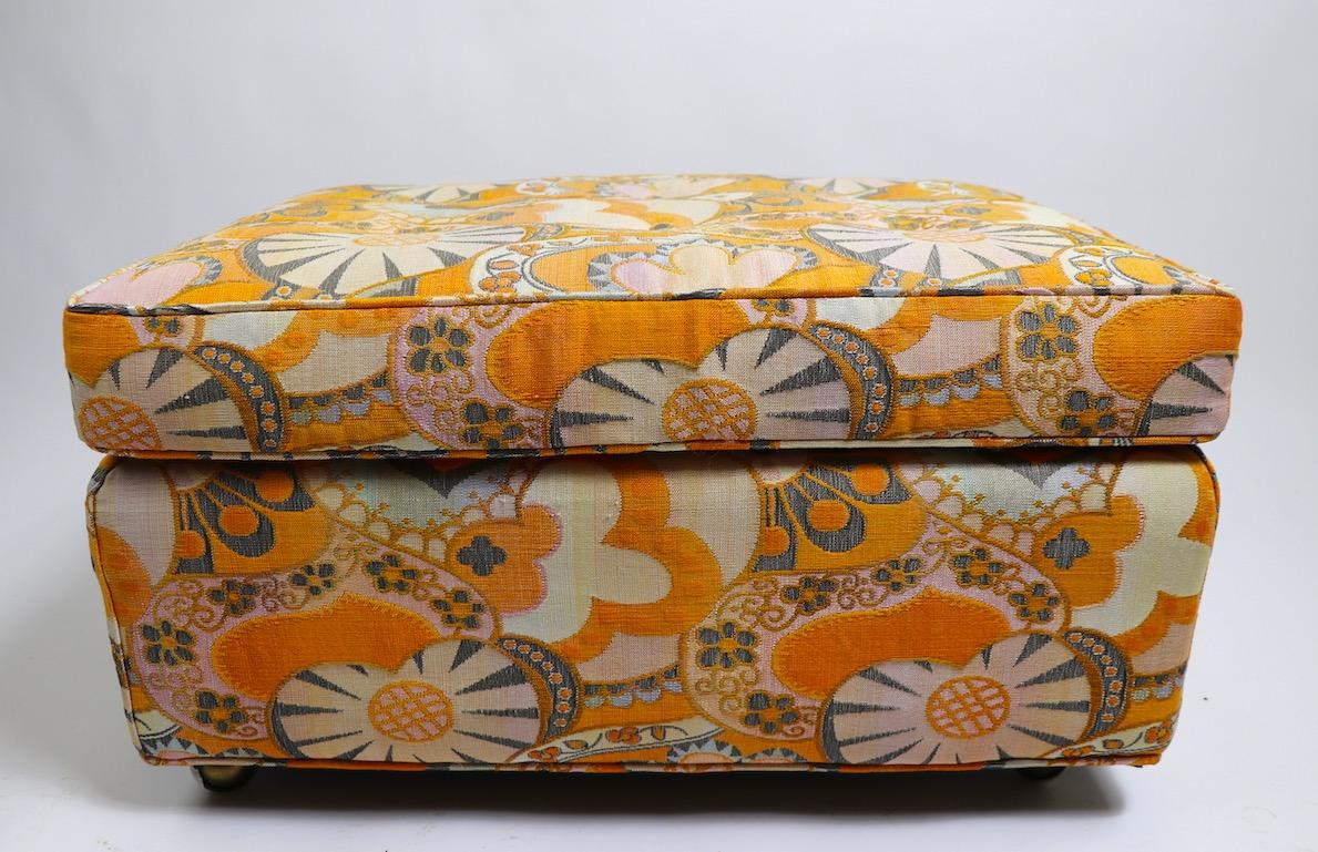 Rectangular ottoman, pouf, footrest in groovy printed fabric, fabric attributed to Jack Lenor Larsen. Exuberant and playful naturalistic pattern, in orange pink, and blue tones. Original, clean condition, ready to use. Fabric is somewhat faded,