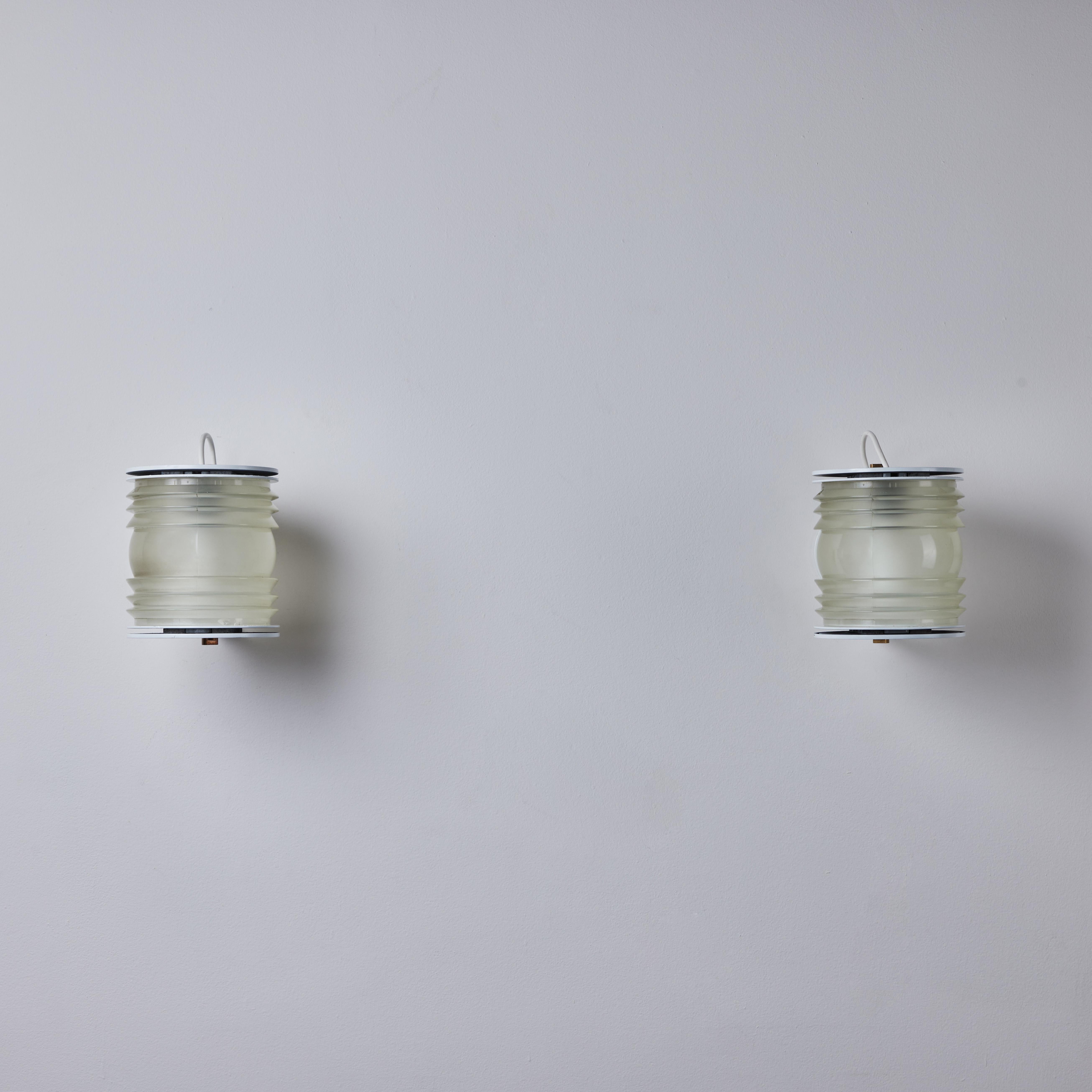 Pair of Model 1151 sconces by Joe Colombo for Oluce. Designed and manufactured in Italy circa 1965. Thick molded glass is housed between an enameled white hickey-shaped bracket. Brass finial details on top and bottom. Rewired for the US. Holds one