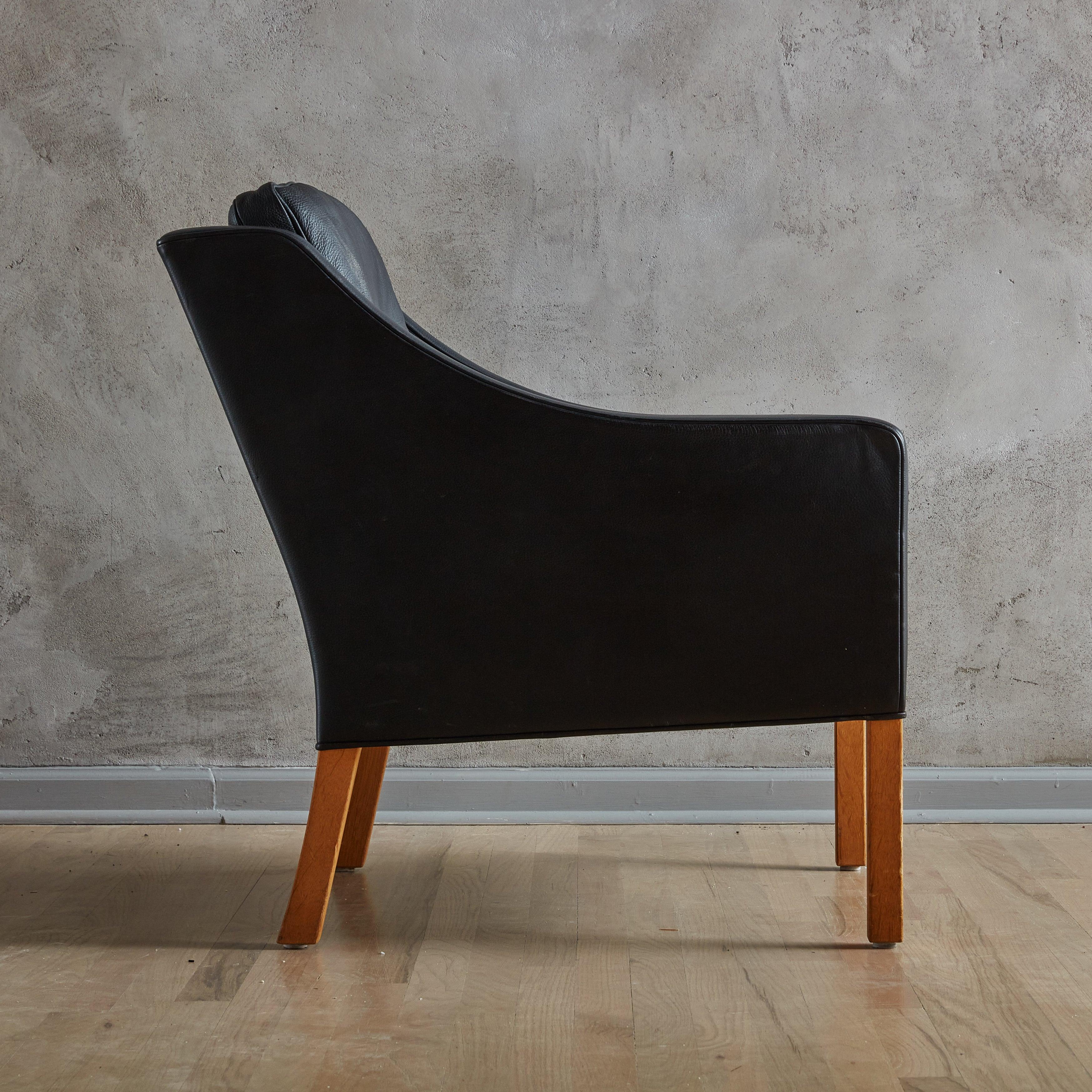 Chaise de salon moderne du milieu du siècle, modèle #2207, recouverte d'un beau cuir noir avec deux coussins amovibles remplis de duvet. La silhouette structurée présente des accoudoirs élégamment inclinés, un dossier incurvé et des pieds