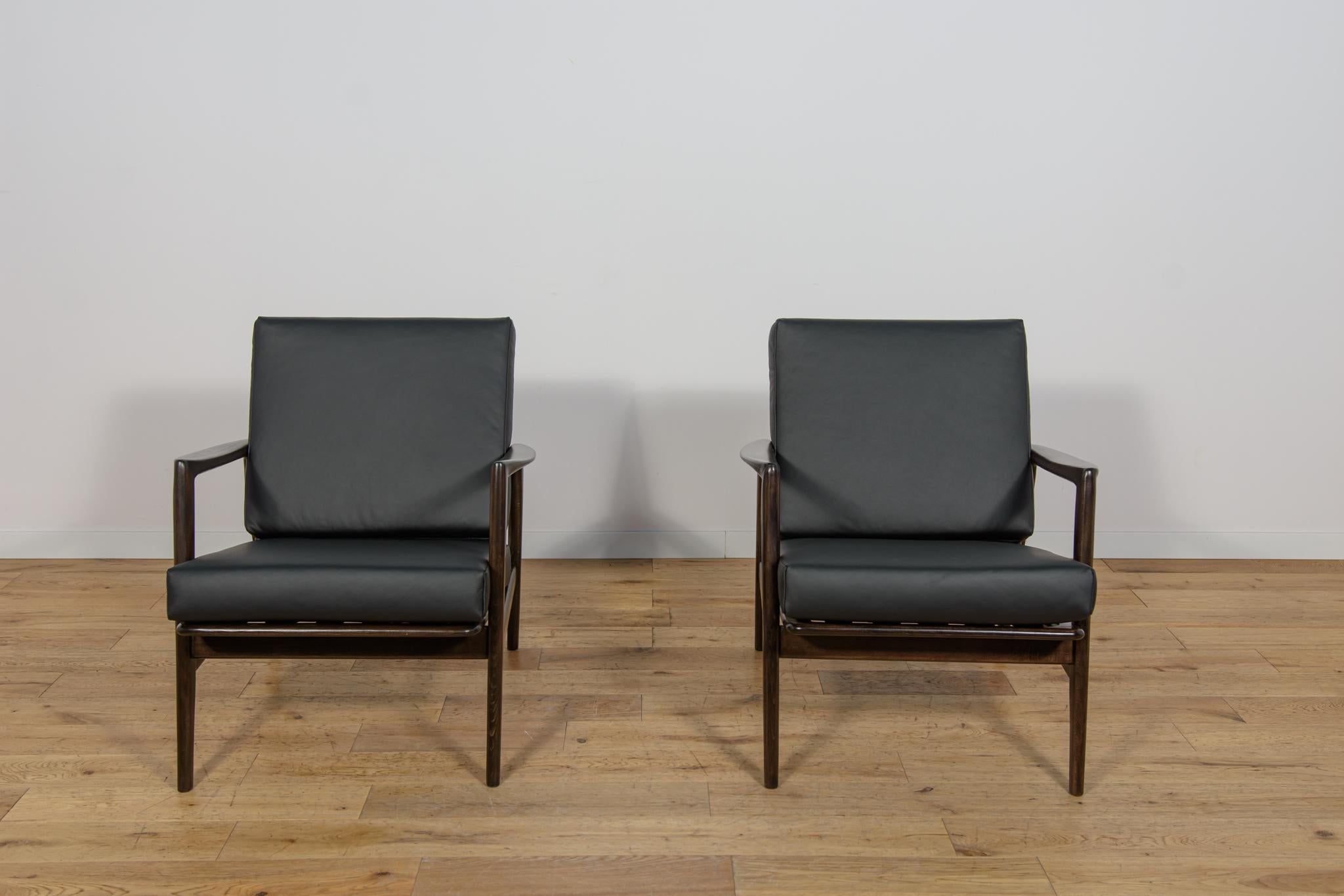 This pair of armchairs was produced by the Polish company Swarzędzka Furniture Factory in 60s.The armchairs have new cushions, reupholstered in a quality new black leather. The beech framehas been cleaned from the old surface, painted with a