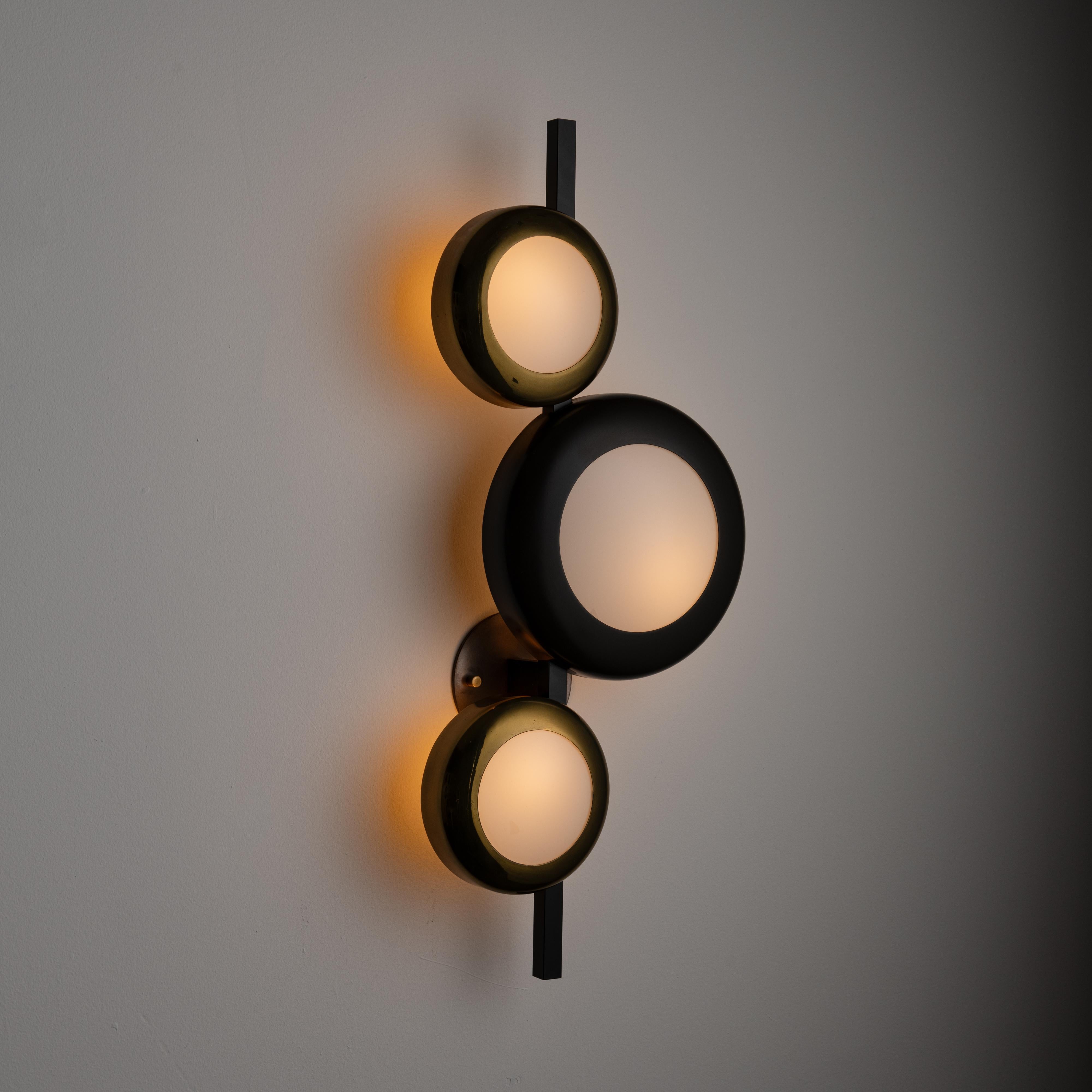 Rare model 580 Sconce by Oscar Torlasco for Lumi. Designed and manufactured in Italy, circa the 1950s. A three-piece surreal-looking wall sconce comprising of black enameled rims containing milk glass lens. Brass hardware and backings to finish this