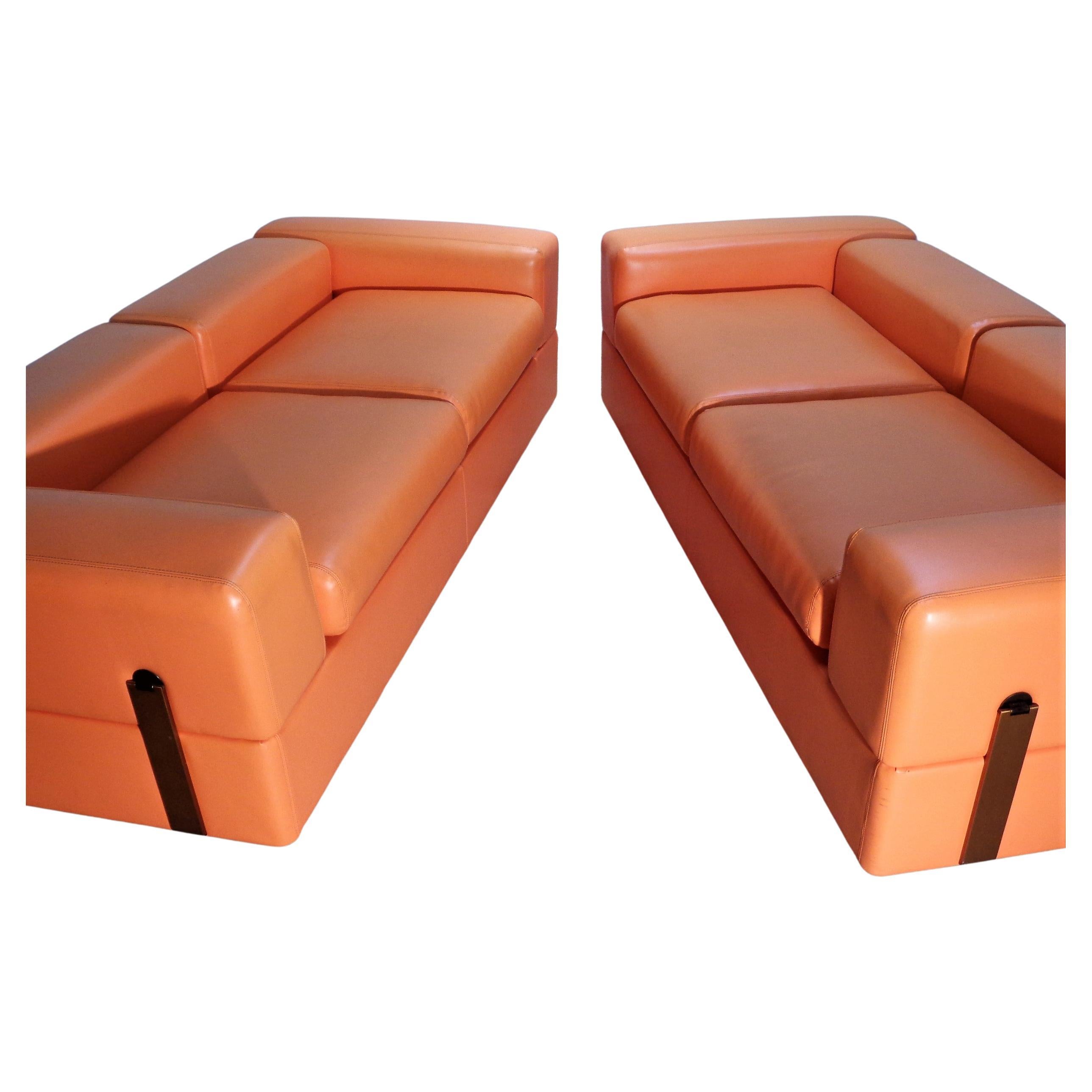 Model 711 daybed sofas by Tito Agnoli for Cinova, c. 1960's, Italy. Original finely stitched creamsicle orange textured vinyl upholstery. Arms and back drop down easily converting sofas to day beds revealing white laminate side tables and back