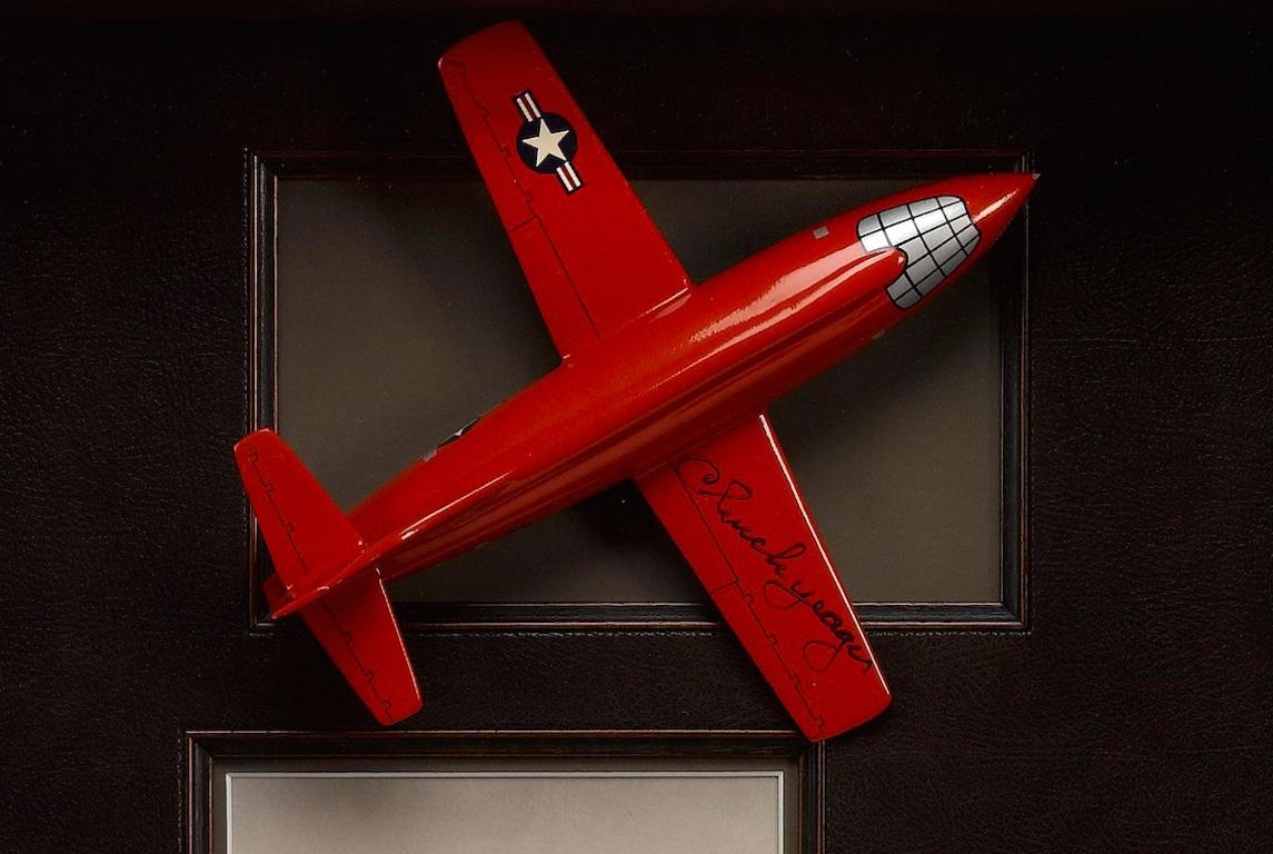 This is a collage featuring a signed model of the Bell X-1 rocket research plane signed by Charles “Chuck” Yeager along the wing. Below the model plane is a photo of Yeager with his historic Bell X-1 and a silver star. All are housed in a custom