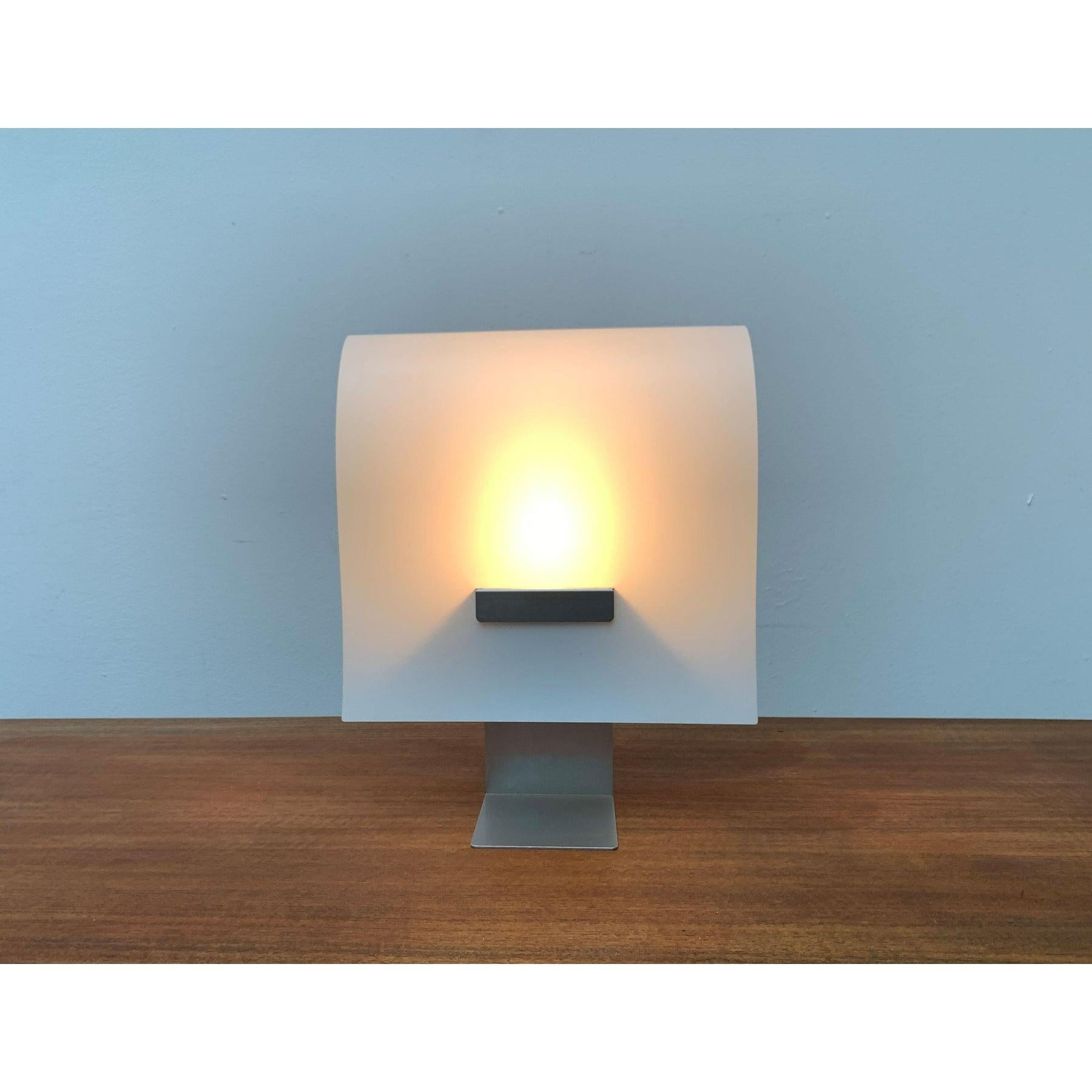 Lampe de table minimaliste basée sur un design de cristina lamiquiz de 1995.

Le design impressionne par son minimalisme et son utilisation de la matérialité. La courbe élégante et douce du diffuseur en plastique est frappante. La surface en