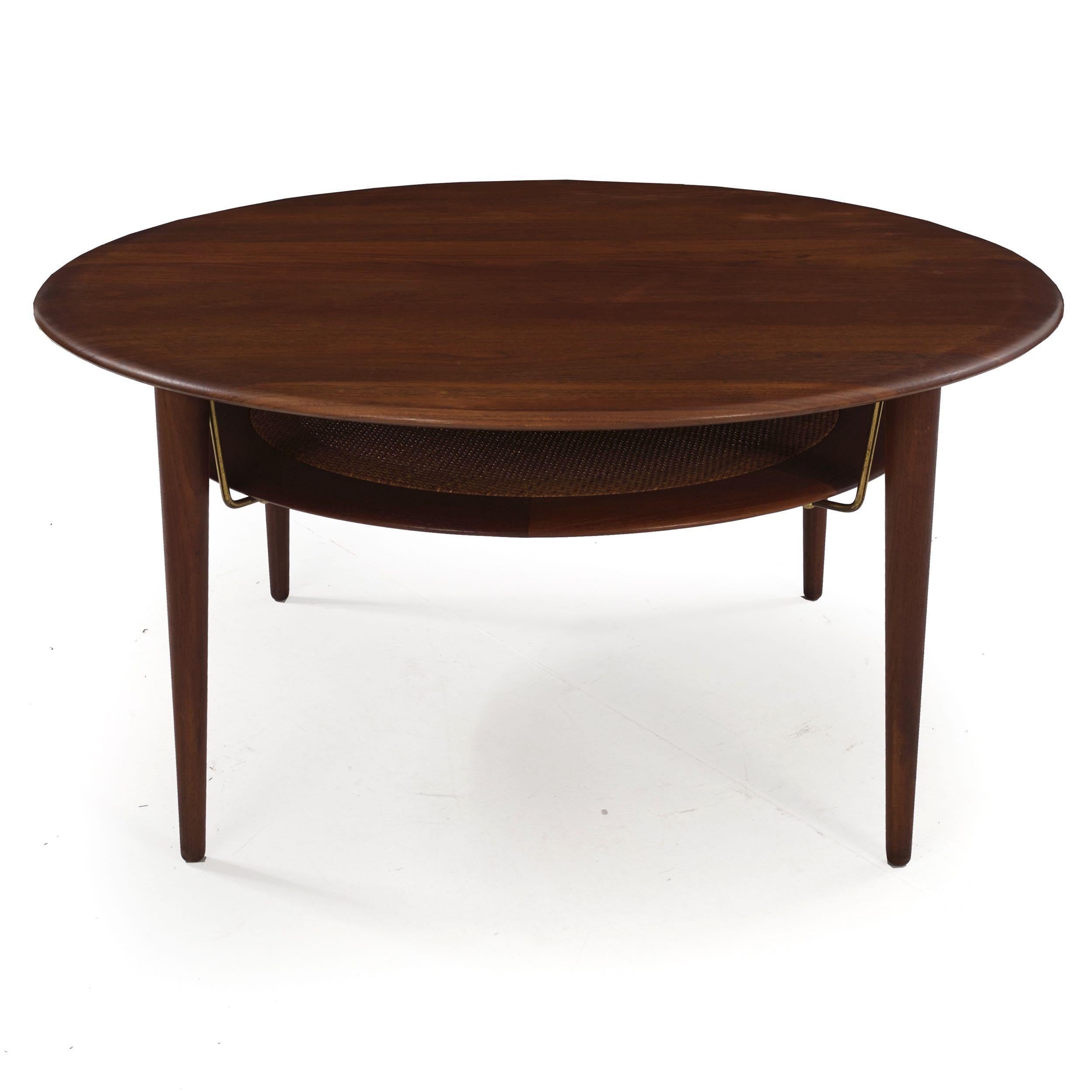 A delightful two-tiered coffee table designed by Peter Hvidt and Orla Mølgaard Nielsen in the 1950s for manufacture by France & Daverkosen, it features a solid teak overall circular profile with a mid-shelf of framed woven wicker surrounded by a