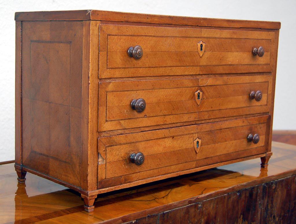 Model furniture, Louis XVI dresser, 1810s. Made of walnut. A rare collector's item of high historical value.

Tied square feet, above three drawers with circumferential ribbon and thread inserts, knobs and heraldic key plates. Sides and top plate
