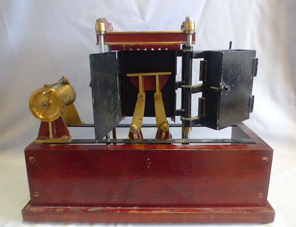 An impressive model of a press or baling machine. The carcase is in mahogany while the working parts are in brass and steel. The goods to be pressed or baled are loaded in to the black containers and power is applied to lift the scissor pressing