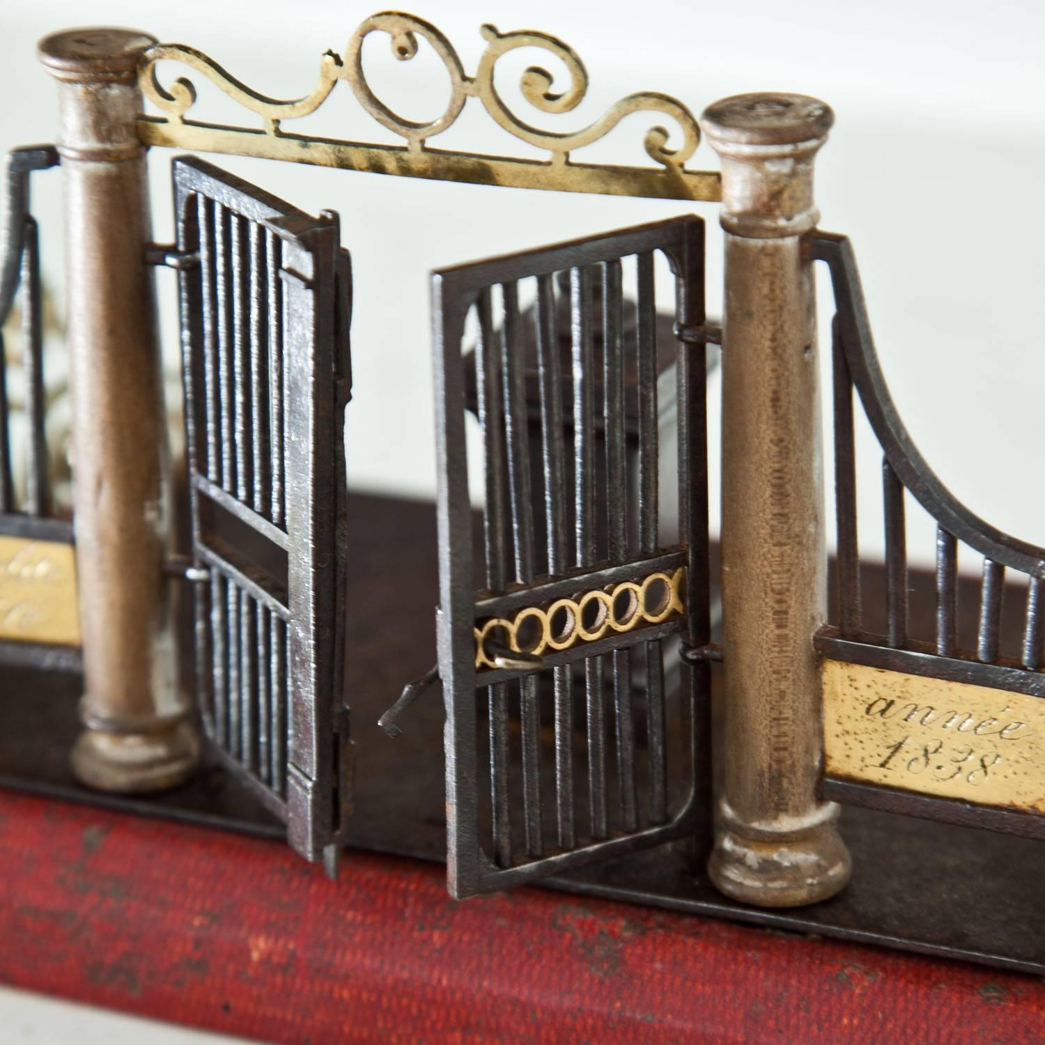 Small model of a gate out of brass and iron with columns and a large double-door. The model is signed Hippolite Barré and dated 1838.