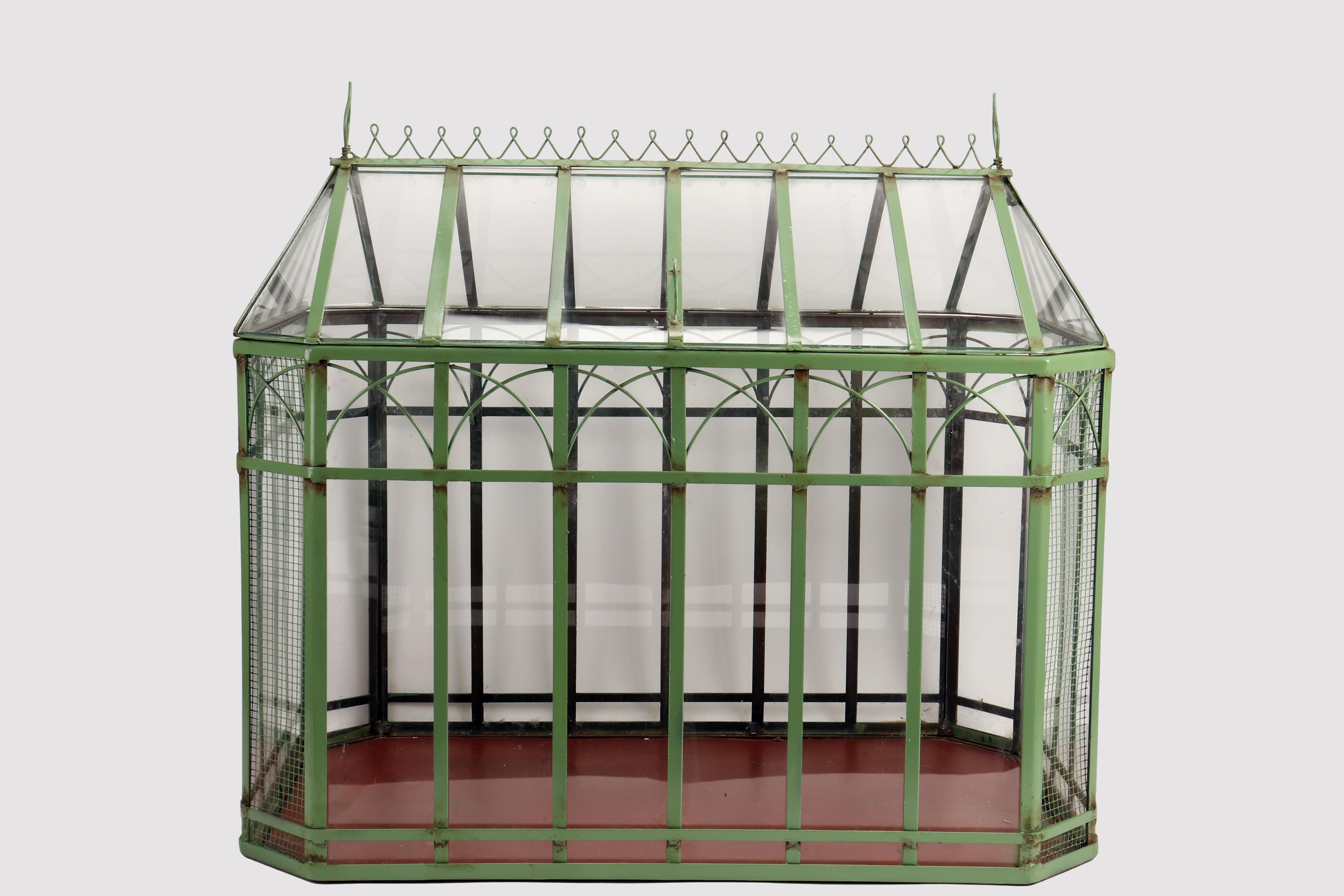 Model of a greenhouse in glass and iron. The greenhouse has an iron base, rectangular in shape, with cut corners. The body of the greenhouse, made of iron and glass, is welded to the base. The edge of the base rises upwards with a proportion that