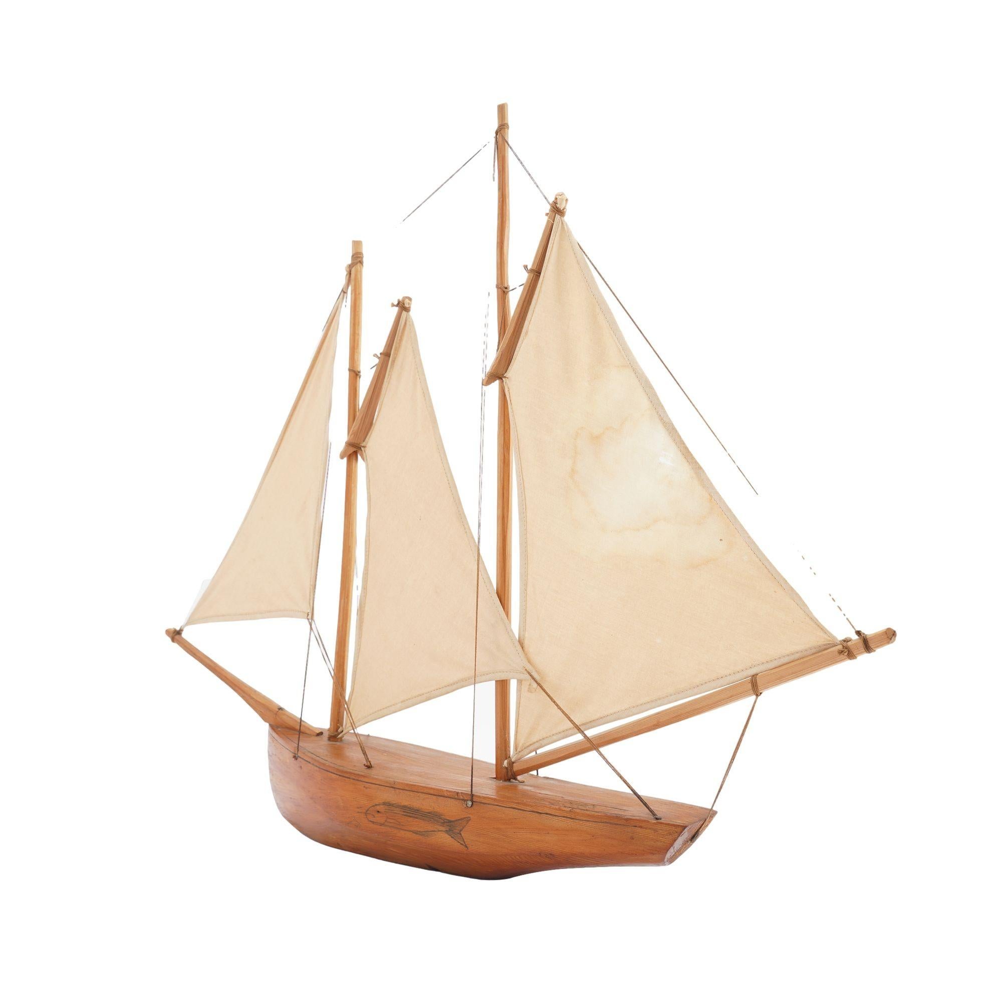 Northern white pine carved model of a New England double masted fishing catch with cotton sails. An engraving of a fish adorns one side of the hull.
American, early 20th century.