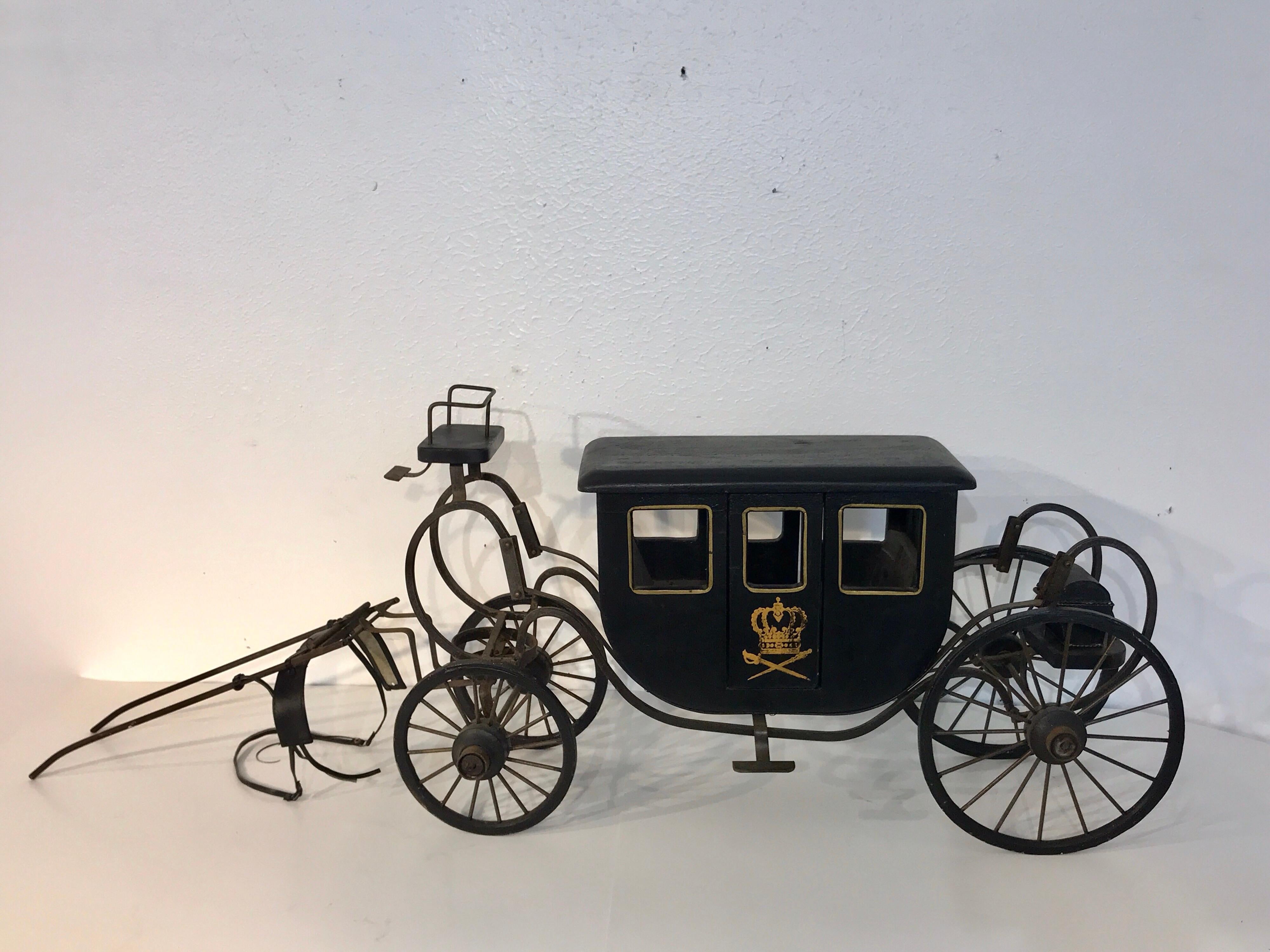 Model of a Royal Carriage, realistically detailed with a carved wood and gilt decorated coach with one working door. Resting on a metal suspension undercarriage and wheels, with leather reins and one removable trunk.
Measures: 27