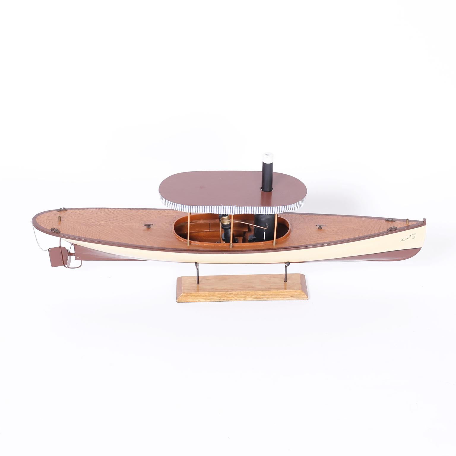 Model of a launch realistically crafted in mahogany, painted on the outside, complete with a steam engine replica, striped awning and presented on a mahogany stand.