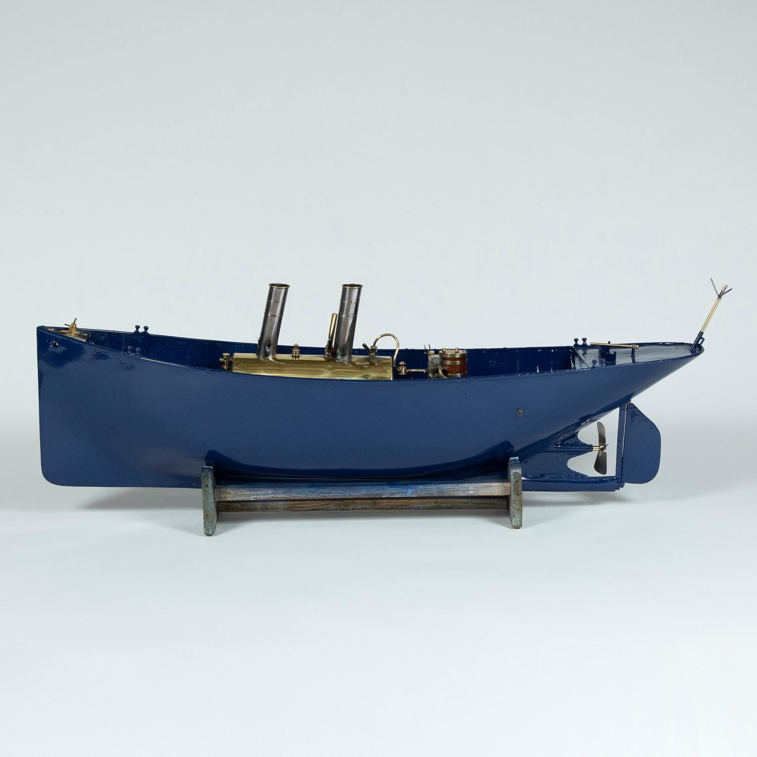 A model of a single screw steamboat, with live-steam engine. 

Painted steel hull with tiller and rudder. 

Brass boiler and burner. Single cylinder vertical lagged marine engine, propeller shaft with forward and reverse, and three blade