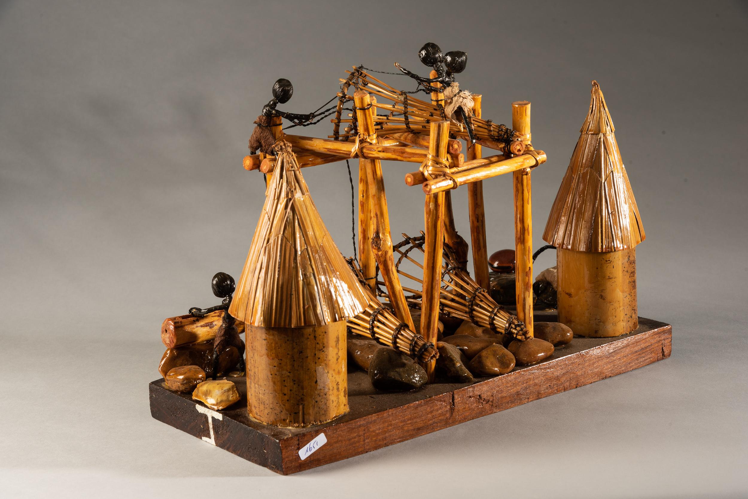 Dies ist ein Touristenmodell einer Wagenia-Fischeranlage aus Holz, Draht und kleinen Steinen. Das Modell steht auf einem Holzsockel; auf der Vorderseite ist 