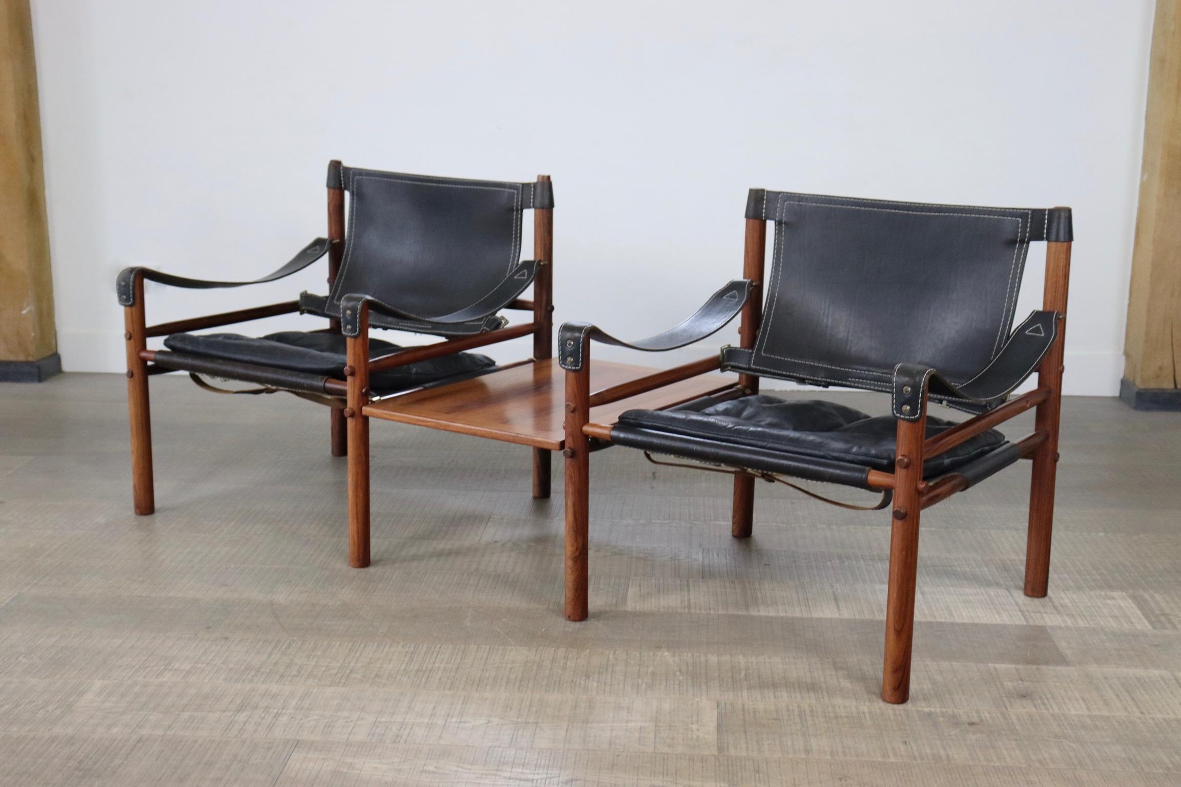 Pair of easy chairs model Sirocco with side table designed by Arne Norell, Produced by Arne Norell AB in Aneby, Sweden. The chairs are made of a rosewood frame and original black leather seating and armrests, with a matching rosewood side table.