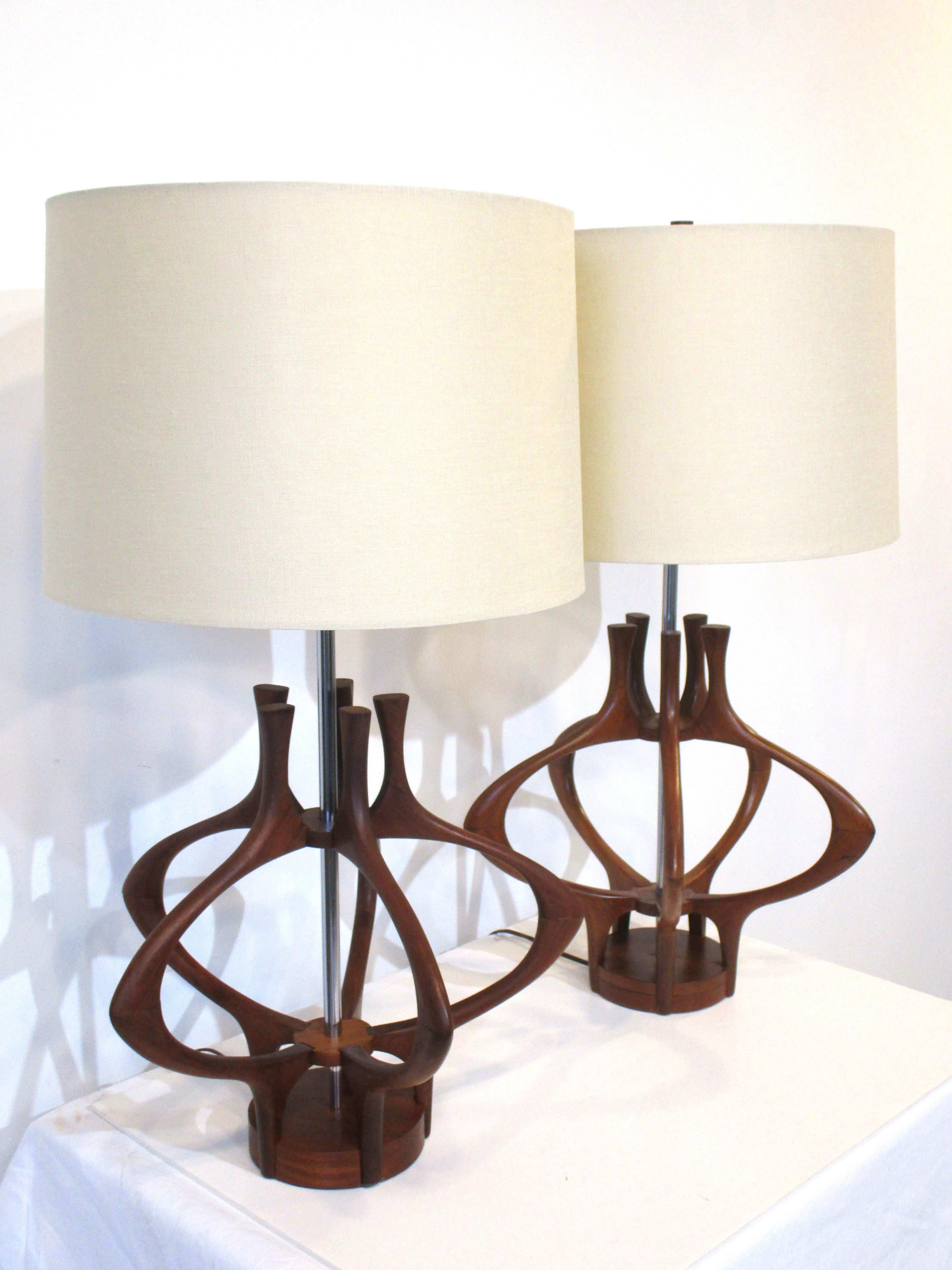 A pair of rare sculptural walnut table lamps with polished metal staff topped with cream toned linen shades. A stunning Danish styled design with the open body letting the light play with the form when lit, attributed to the Modeline Lighting