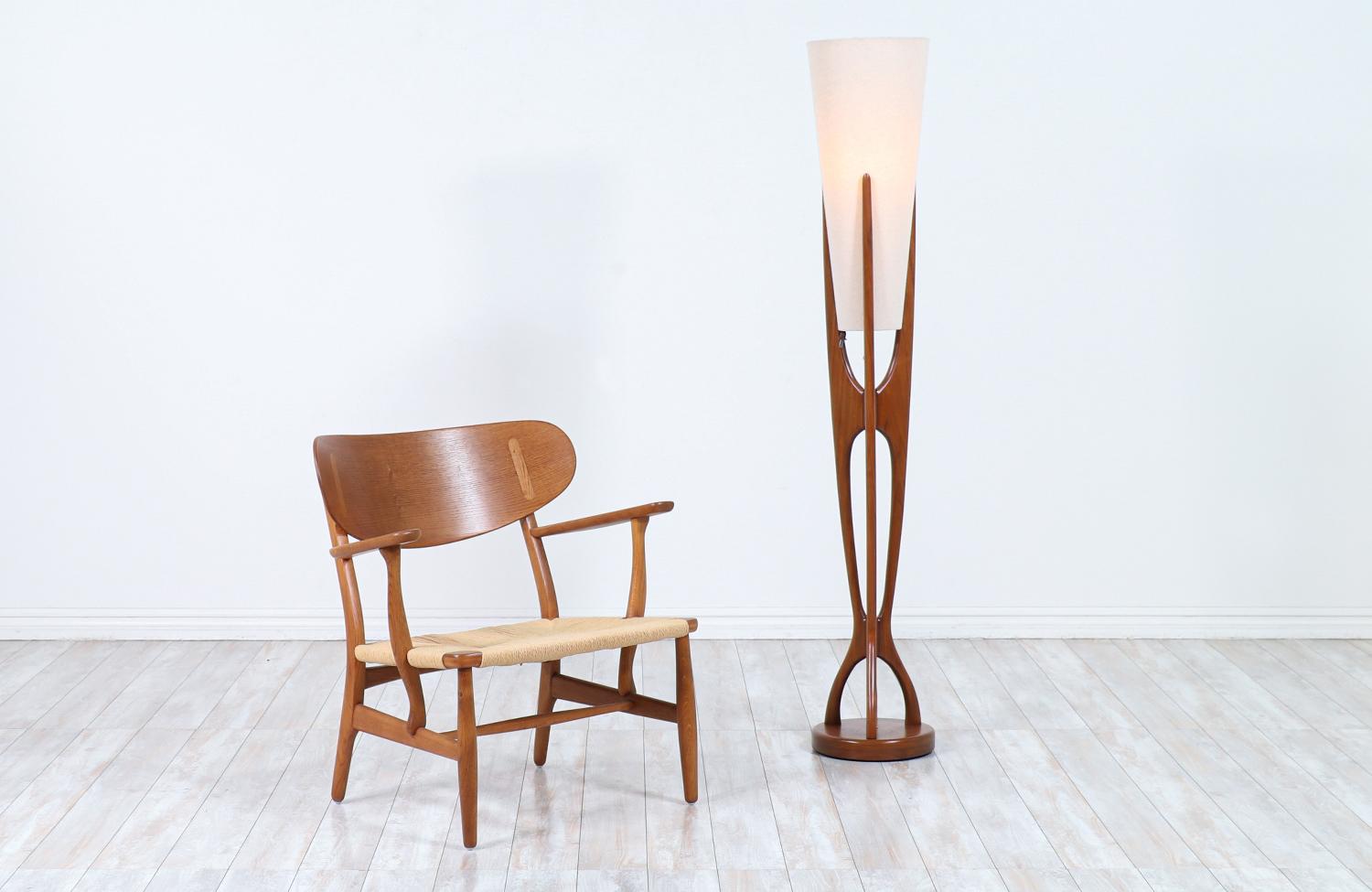Stunning sculpted modern floor lamp designed and manufactured by Modeline of California in the United States circa 1960s. This rare floor lamp is comprised of a carved walnut wood frame that connects from the top to the rounded base creating a